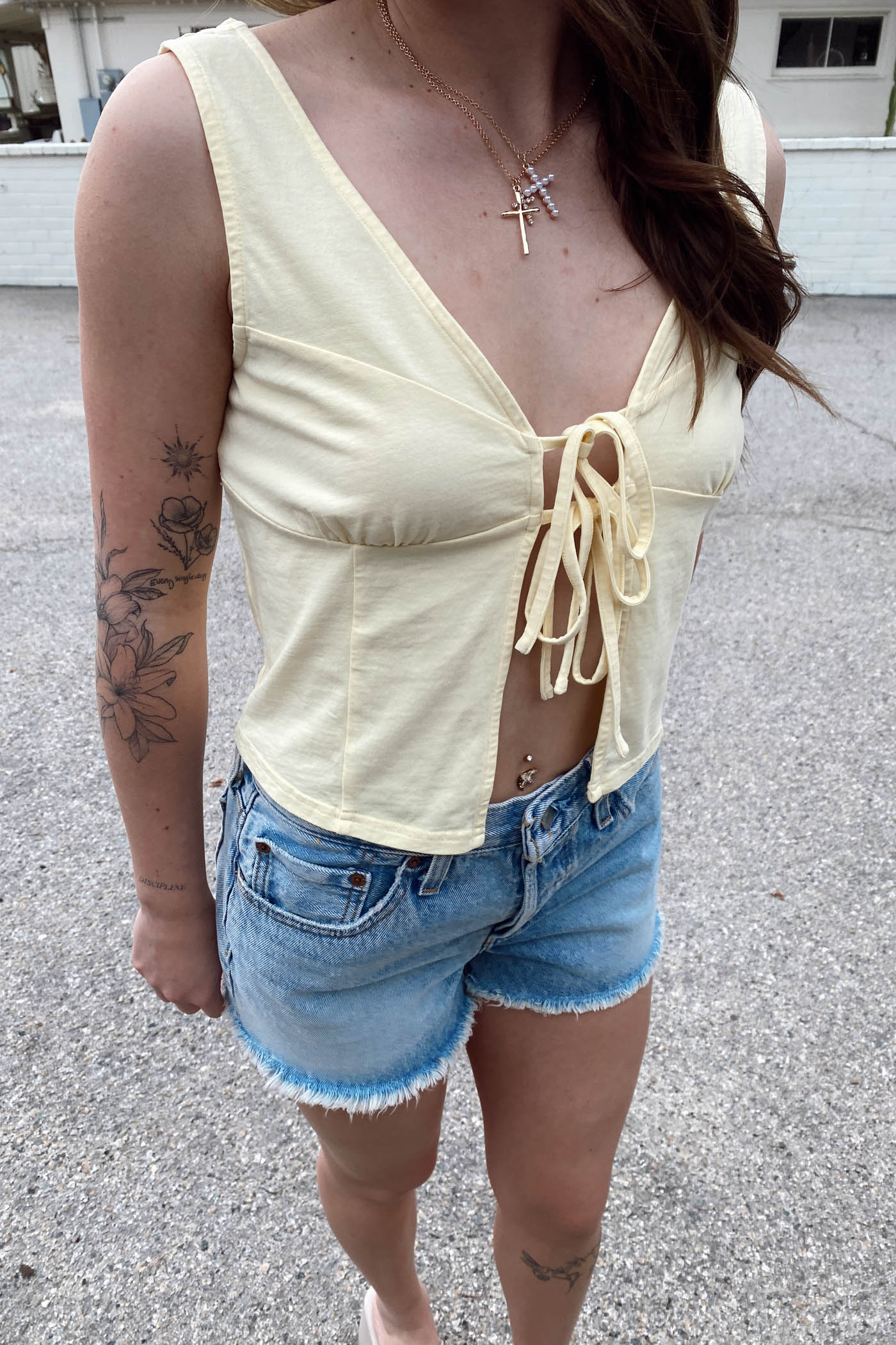Person wearing a light yellow sleeveless top and denim shorts outdoors.