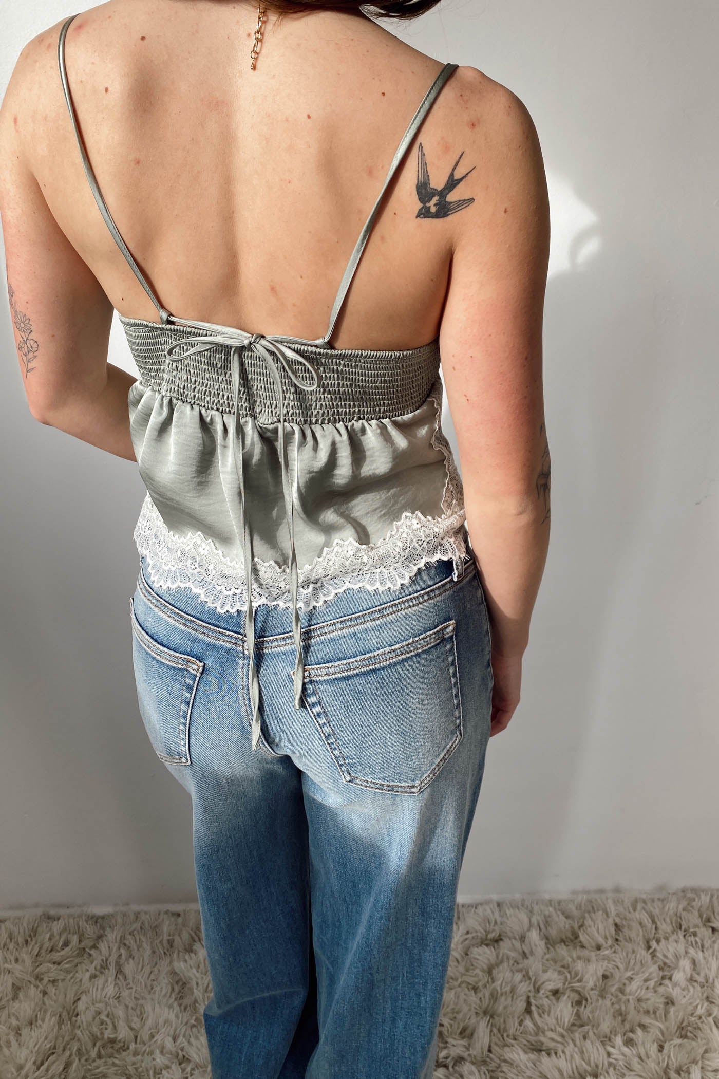 Person wearing a gray top with lace trim and blue jeans against a plain background