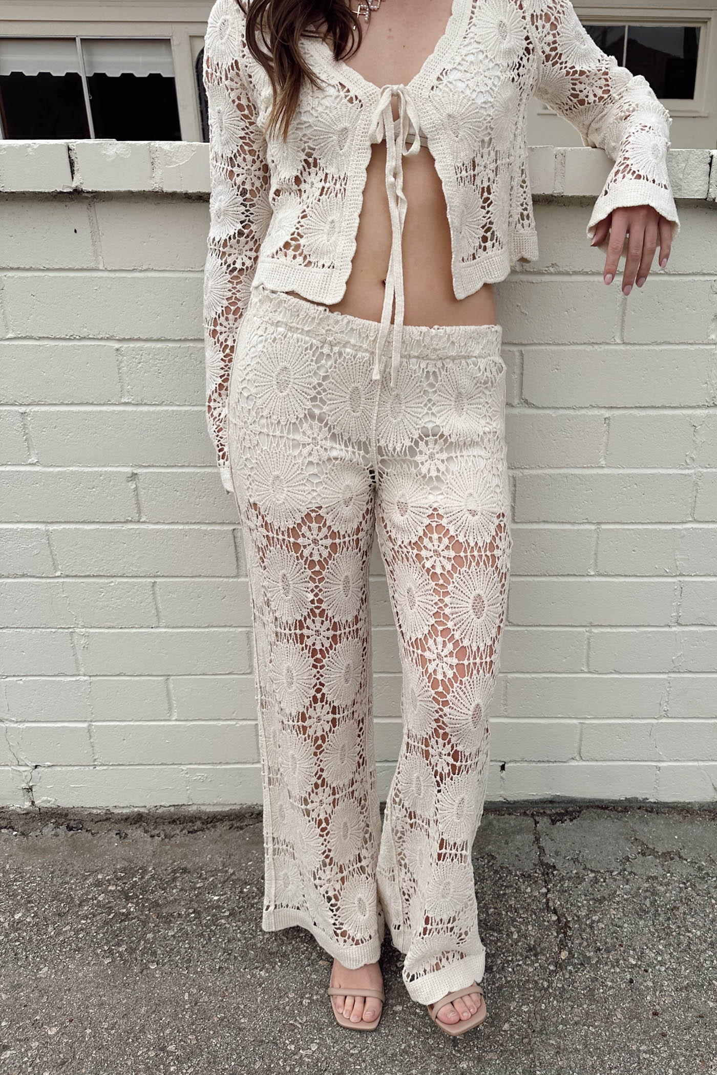 Person wearing a white lace outfit standing against a light gray brick wall.