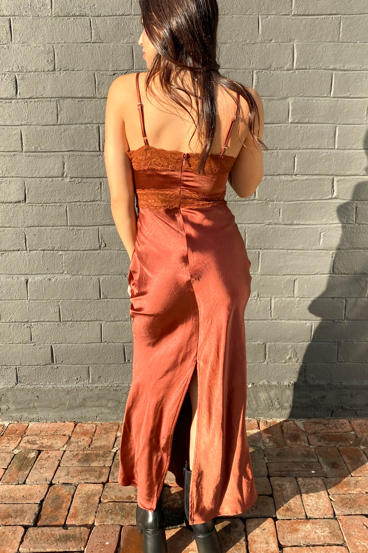 Woman wearing a rust-colored dress standing against a brick wall.