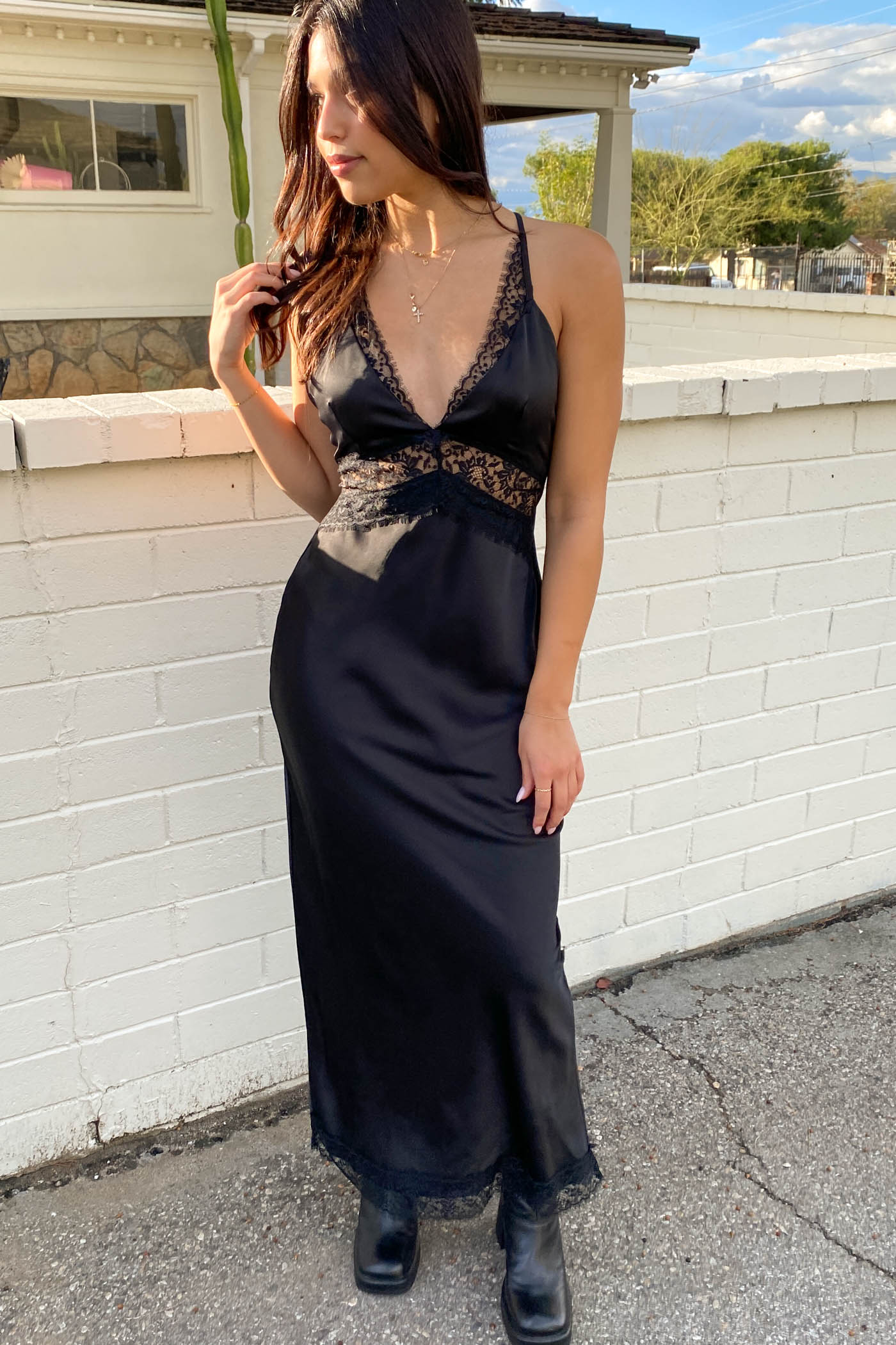 Woman wearing a black dress with lace details standing against a white wall.