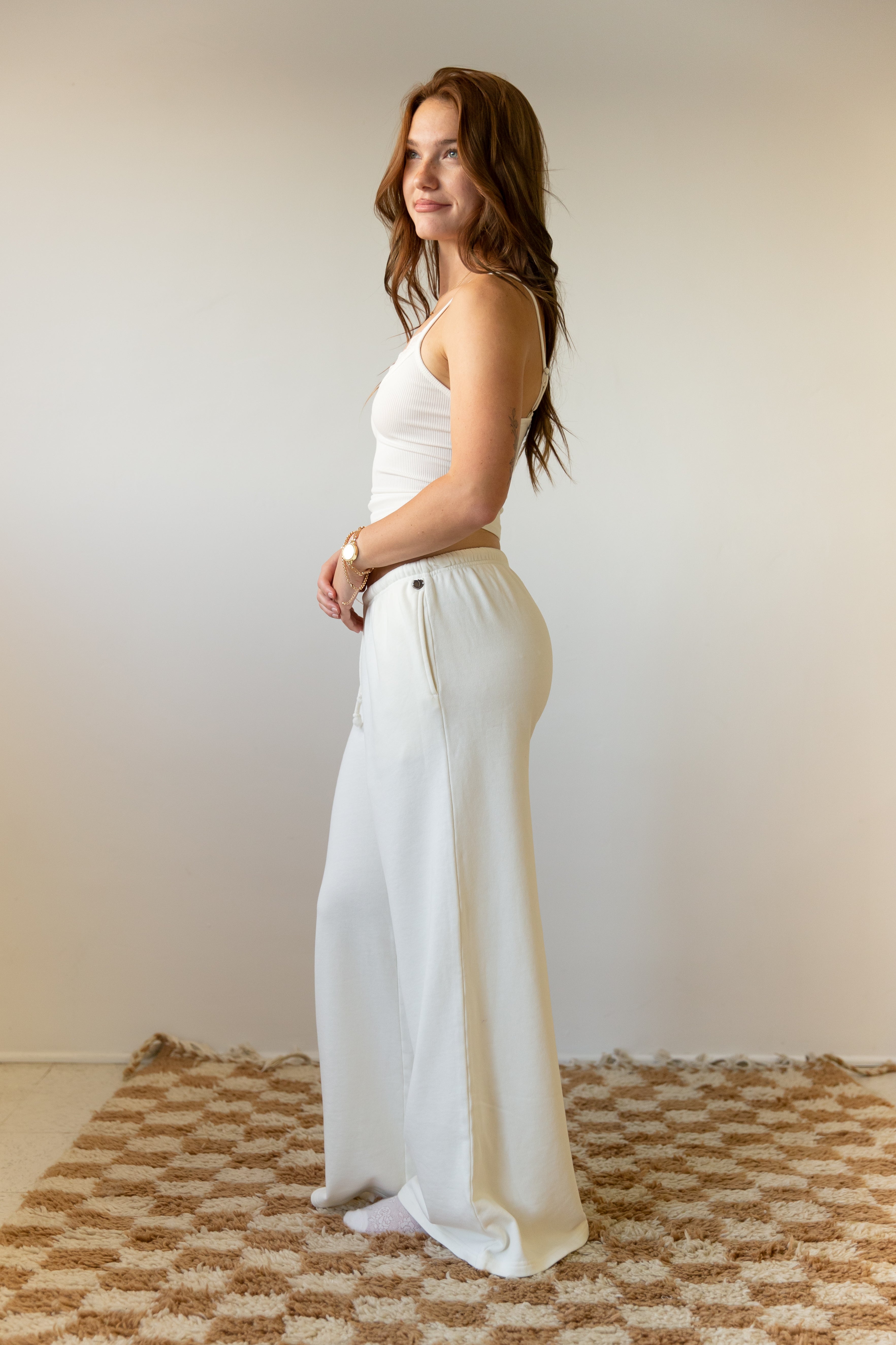 Woman wearing a white sleeveless top and wide-leg pants standing on a patterned rug.