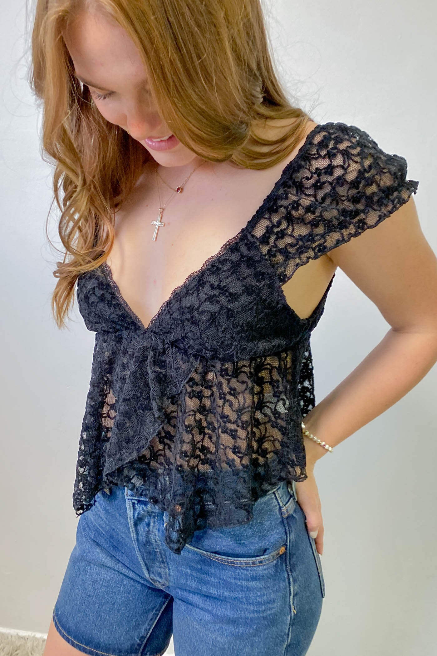 Woman wearing a black lace top and blue shorts against a white background