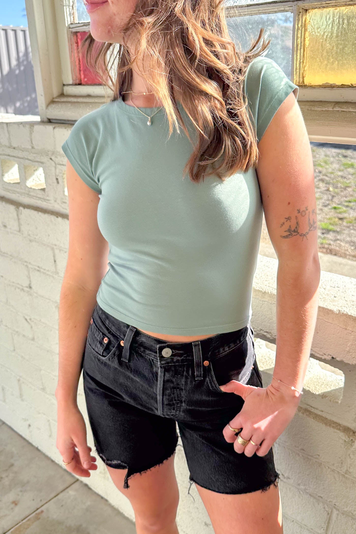Person wearing a light green crop top and black shorts standing on a balcony.