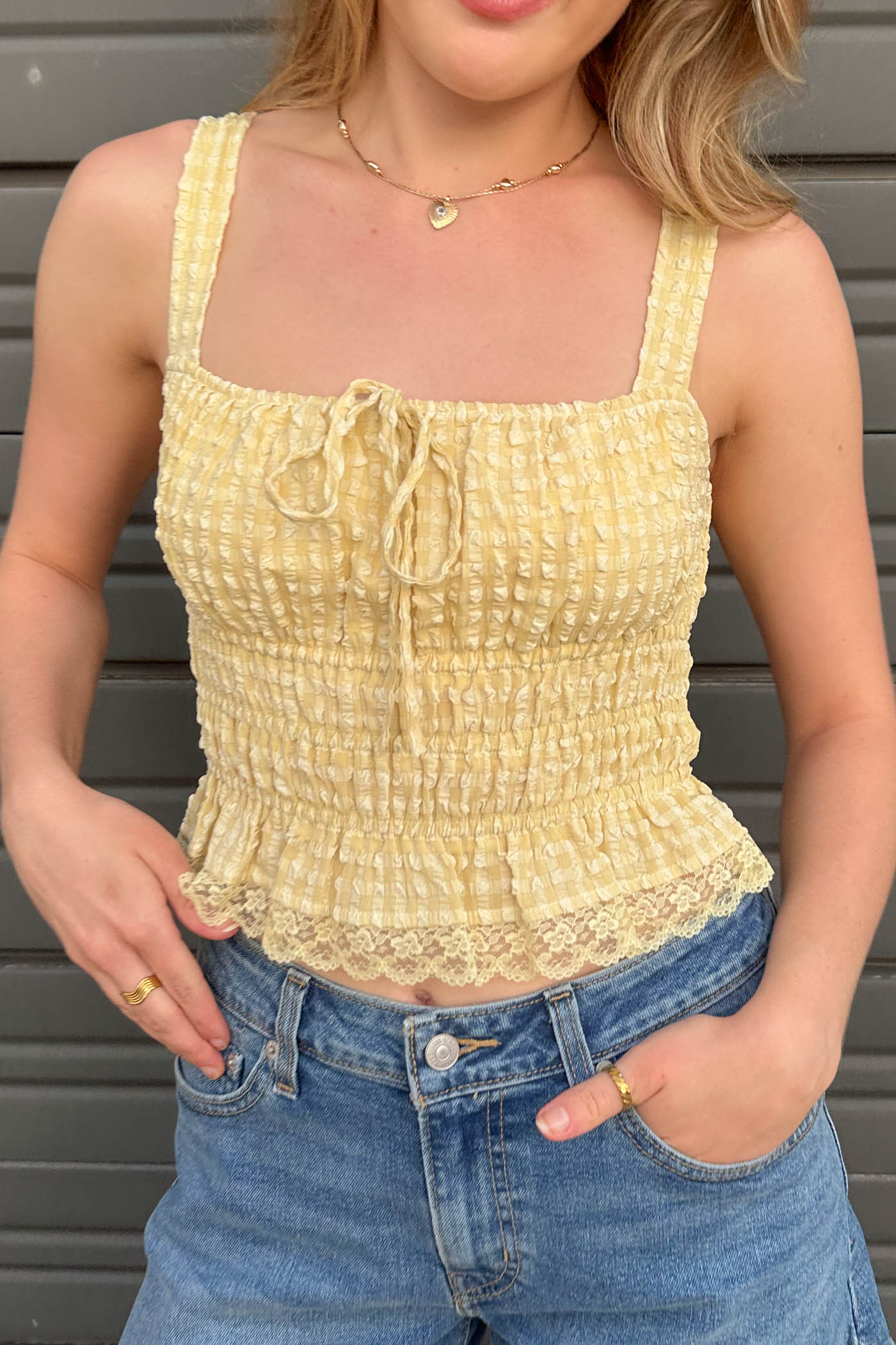 Person wearing a yellow textured top and blue jeans against a gray background