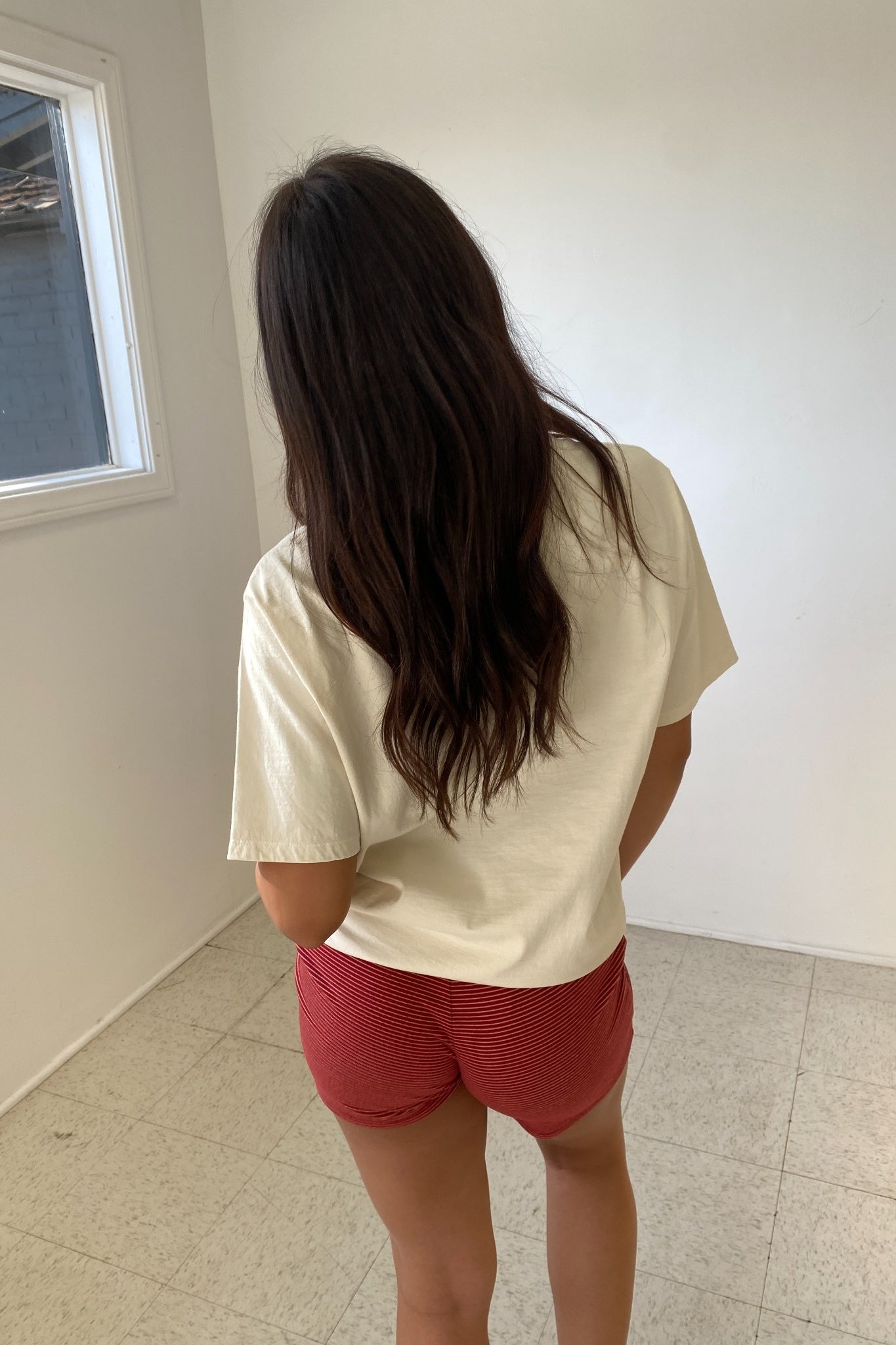 Person wearing a white t-shirt and red shorts standing in a room with a window.