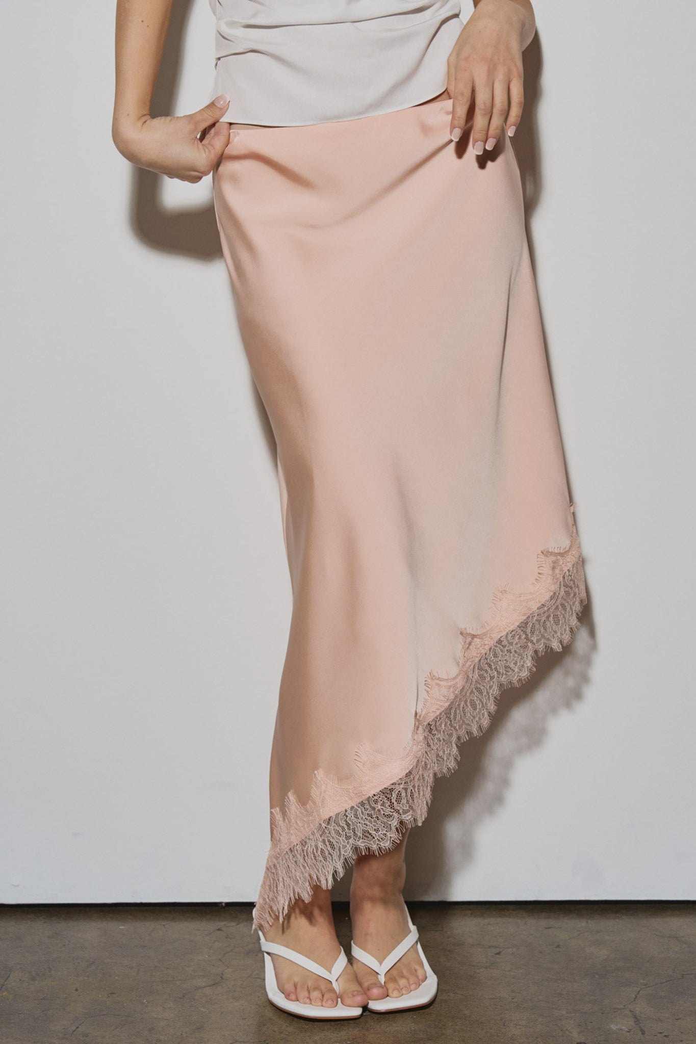 Person wearing a light pink satin skirt with lace trim on a plain background