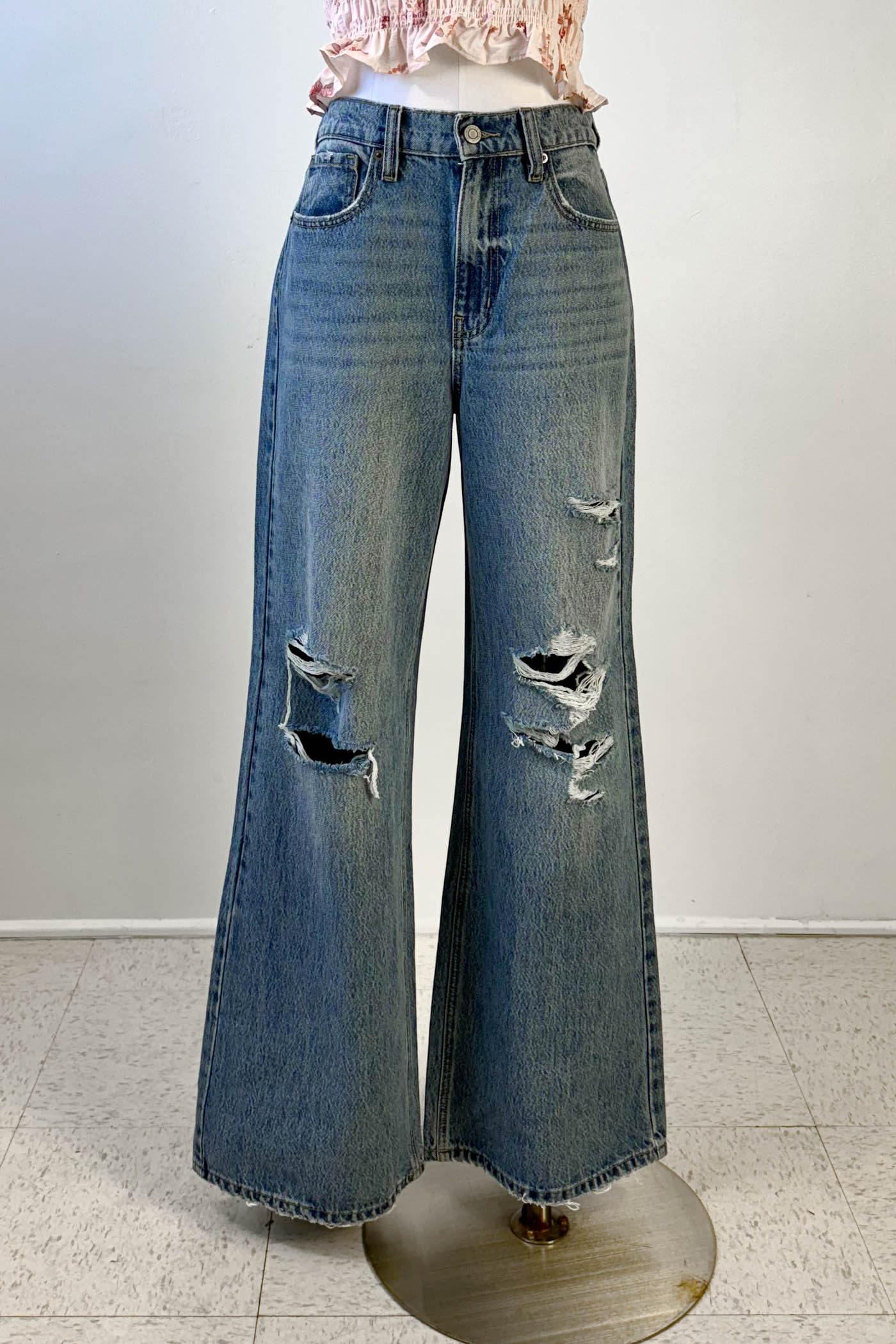 Distressed blue jeans on a mannequin against a white background