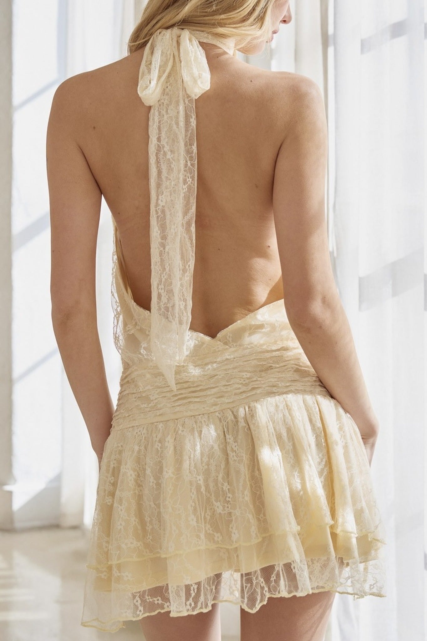 Woman wearing a delicate lace dress with a sheer back panel in a softly lit room.