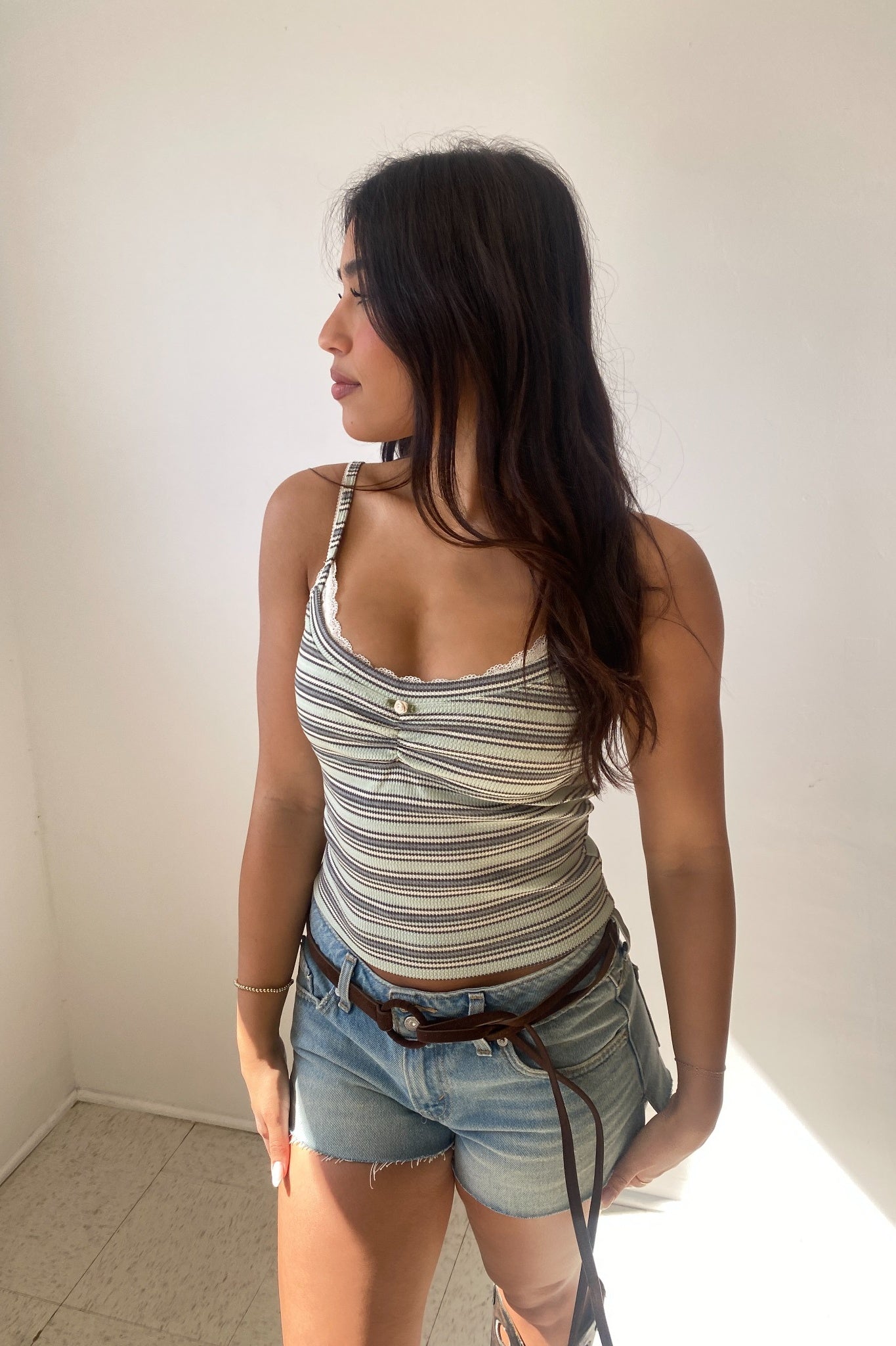 Woman wearing a striped tank top and denim shorts against a plain wall.