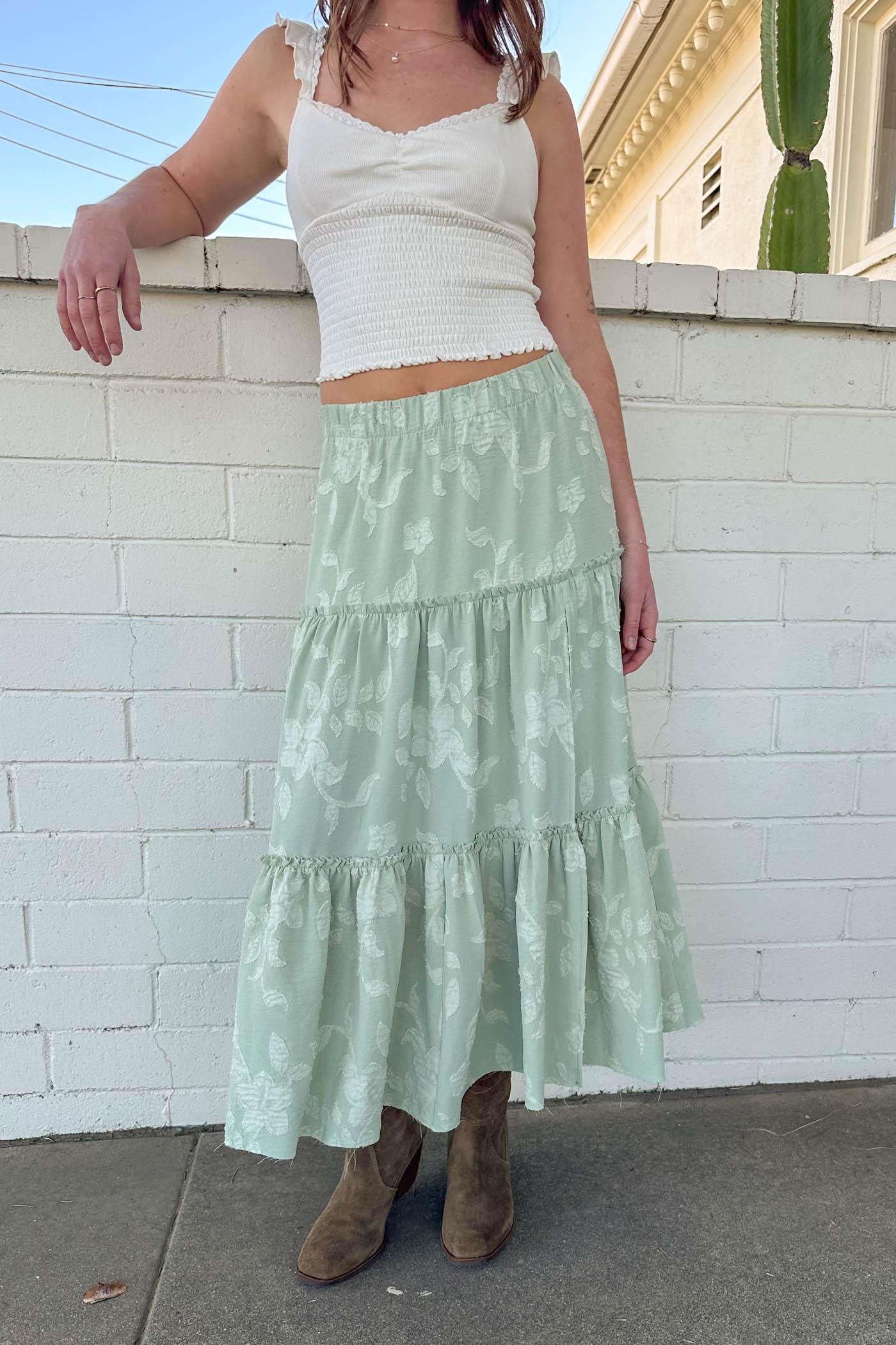 Person wearing a white top and light green skirt against a white brick wall.