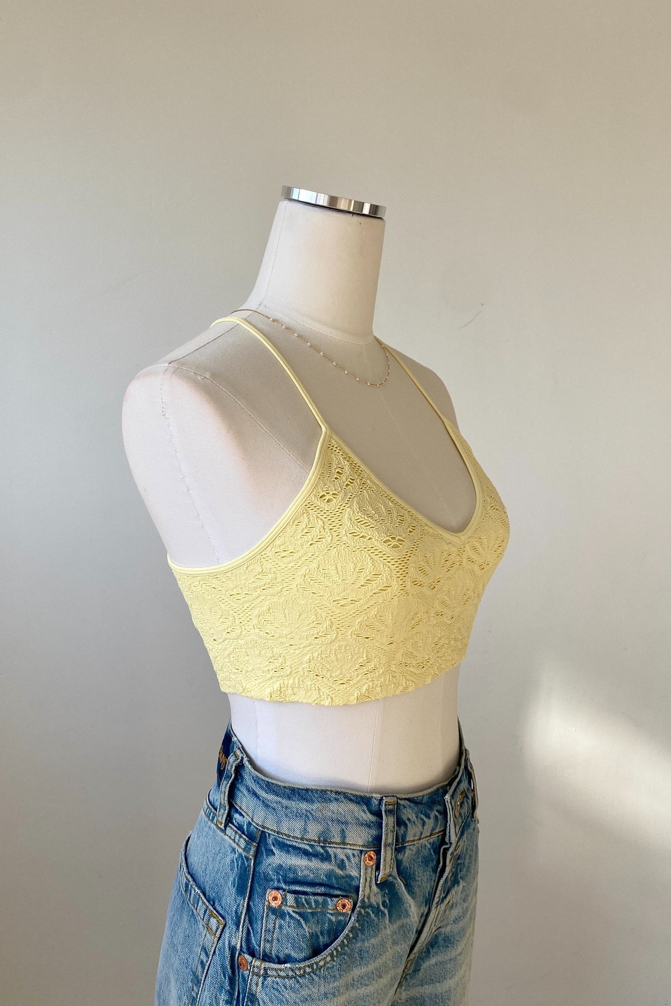 Yellow lace crop top on a mannequin with a plain background