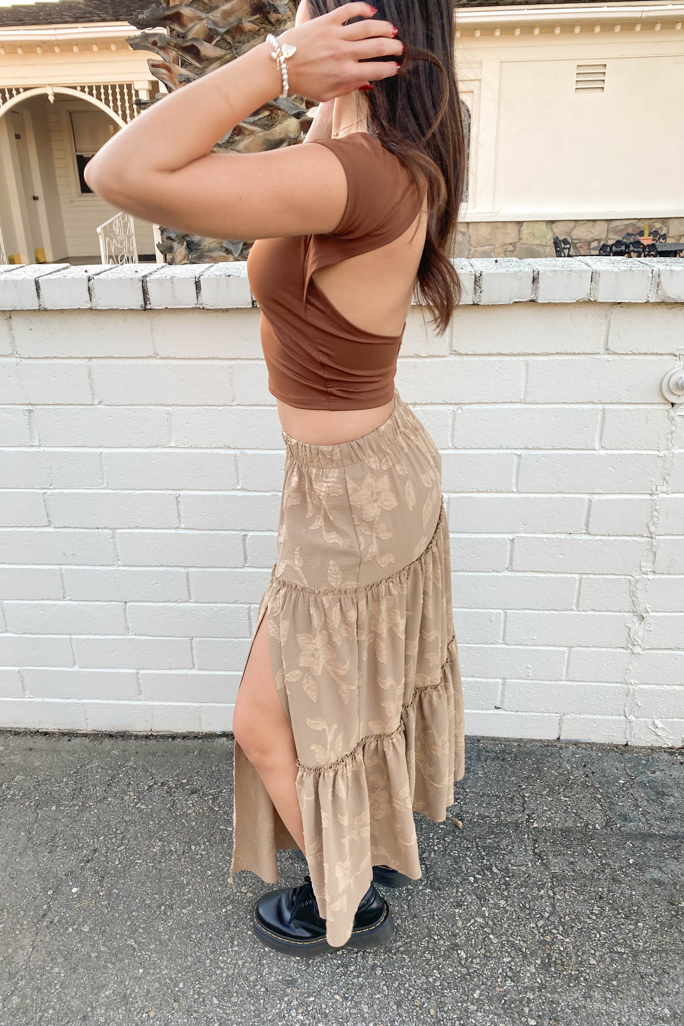 Woman wearing a brown crop top and beige skirt against a white brick wall.