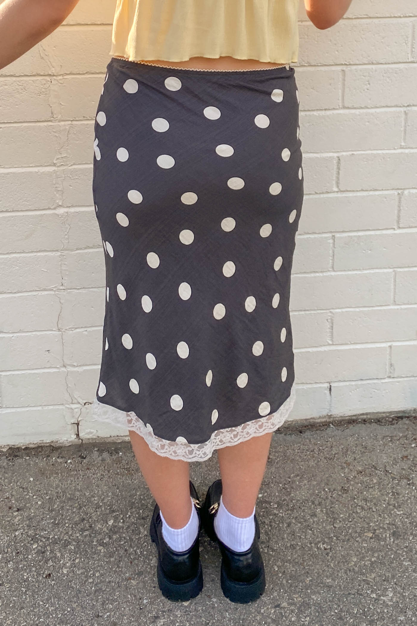 Person wearing a black polka dot skirt with a white brick wall background