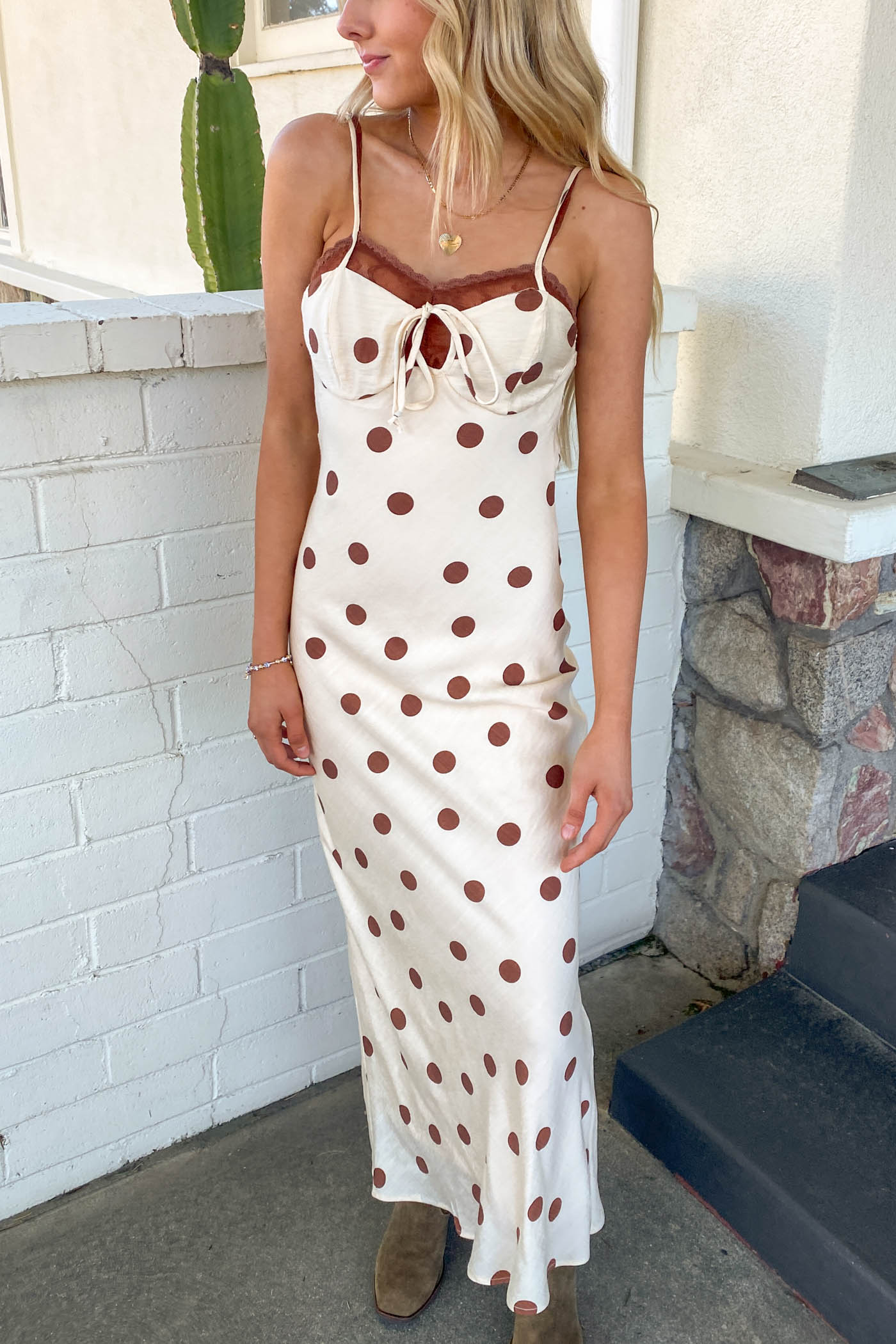 Girl wearing a cream Polka Dotted Maxi Dress standing in front of a brick wall.