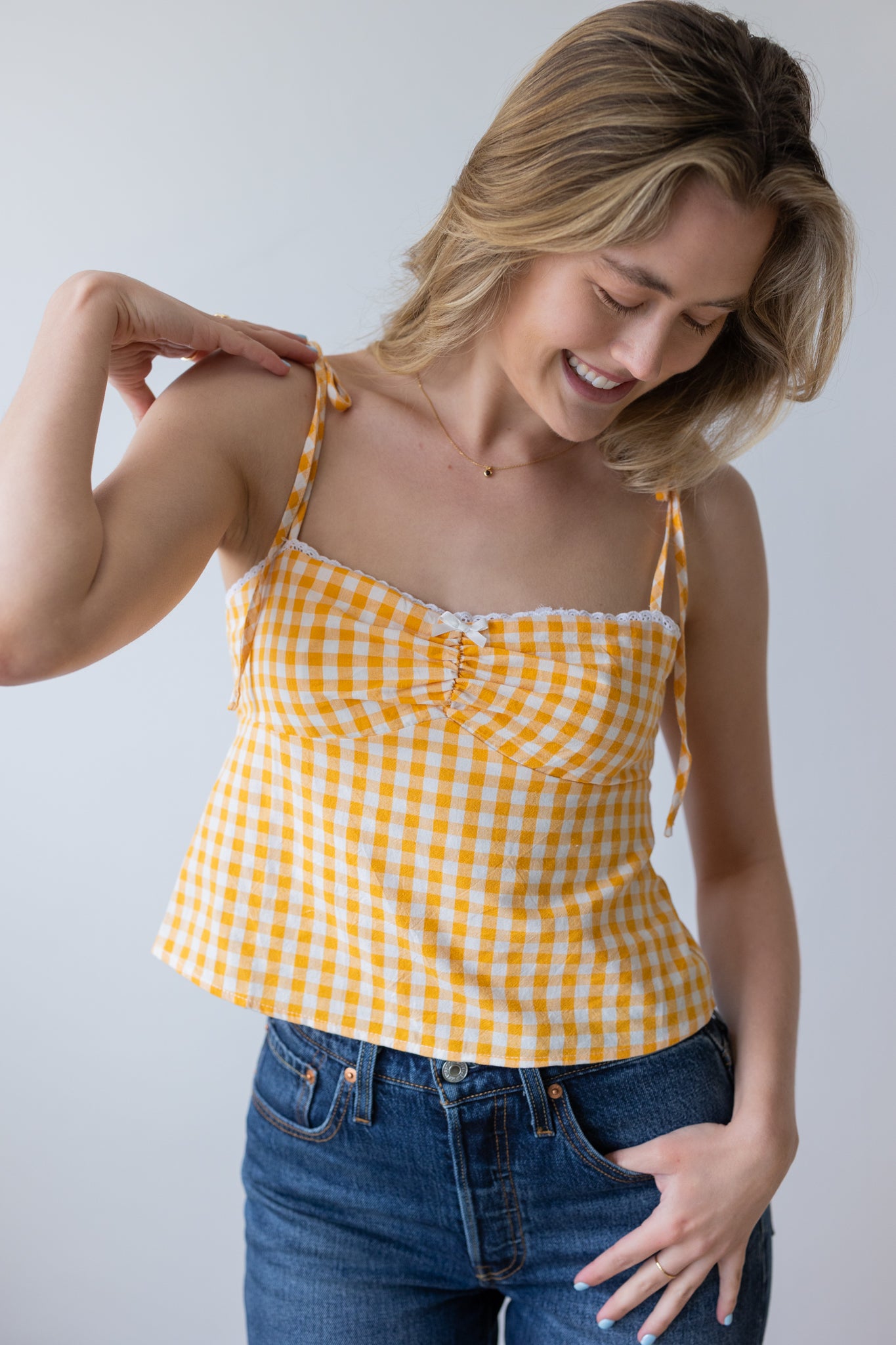 Woman wearing a yellow checkered top and blue jeans against a plain background