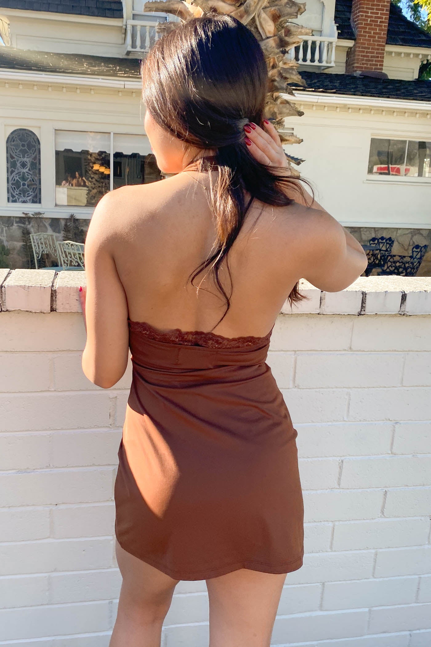 Woman in a brown dress standing on a balcony with a house in the background