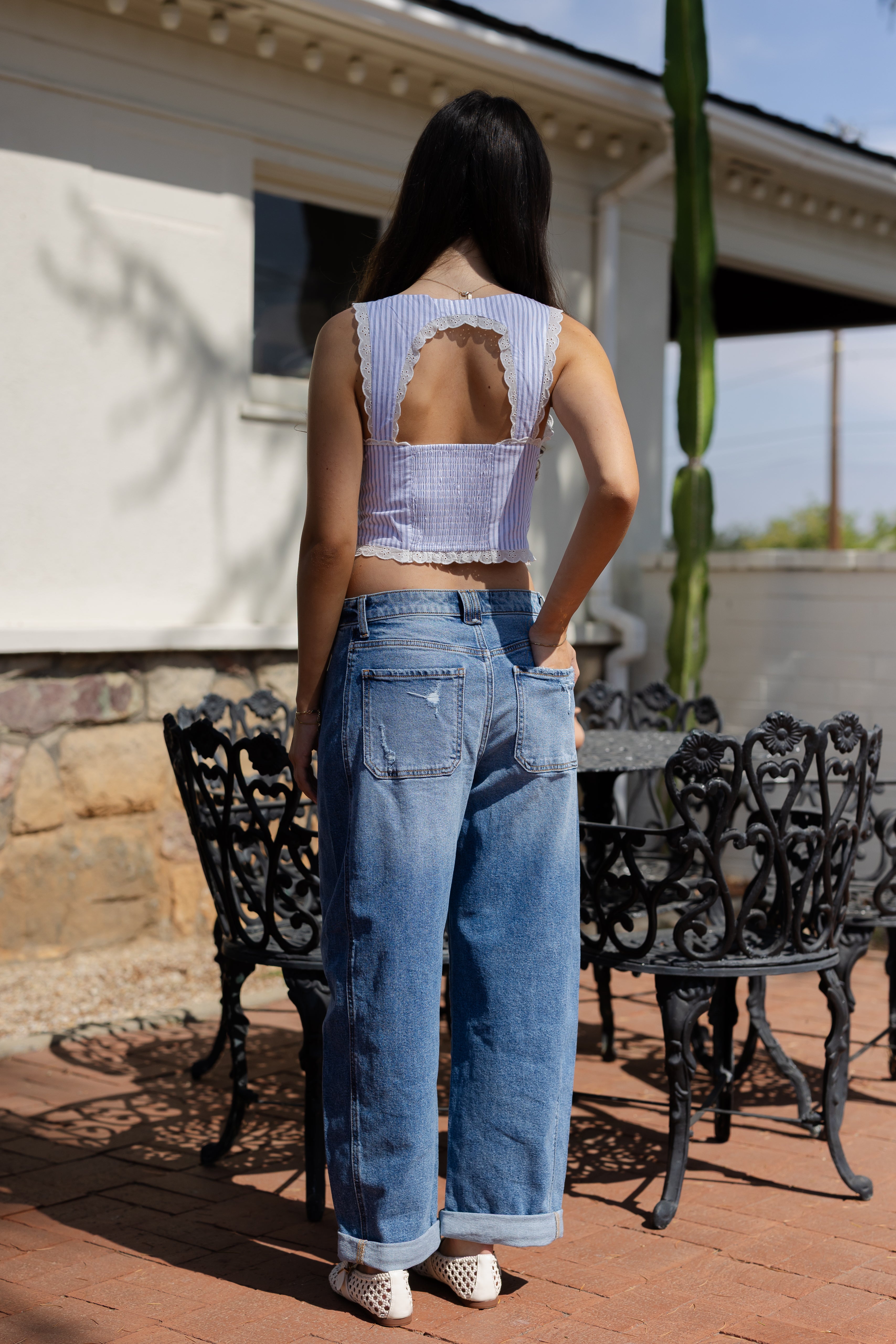 Person wearing a distressed denim outfit standing outdoors with a building and cactus in the background.