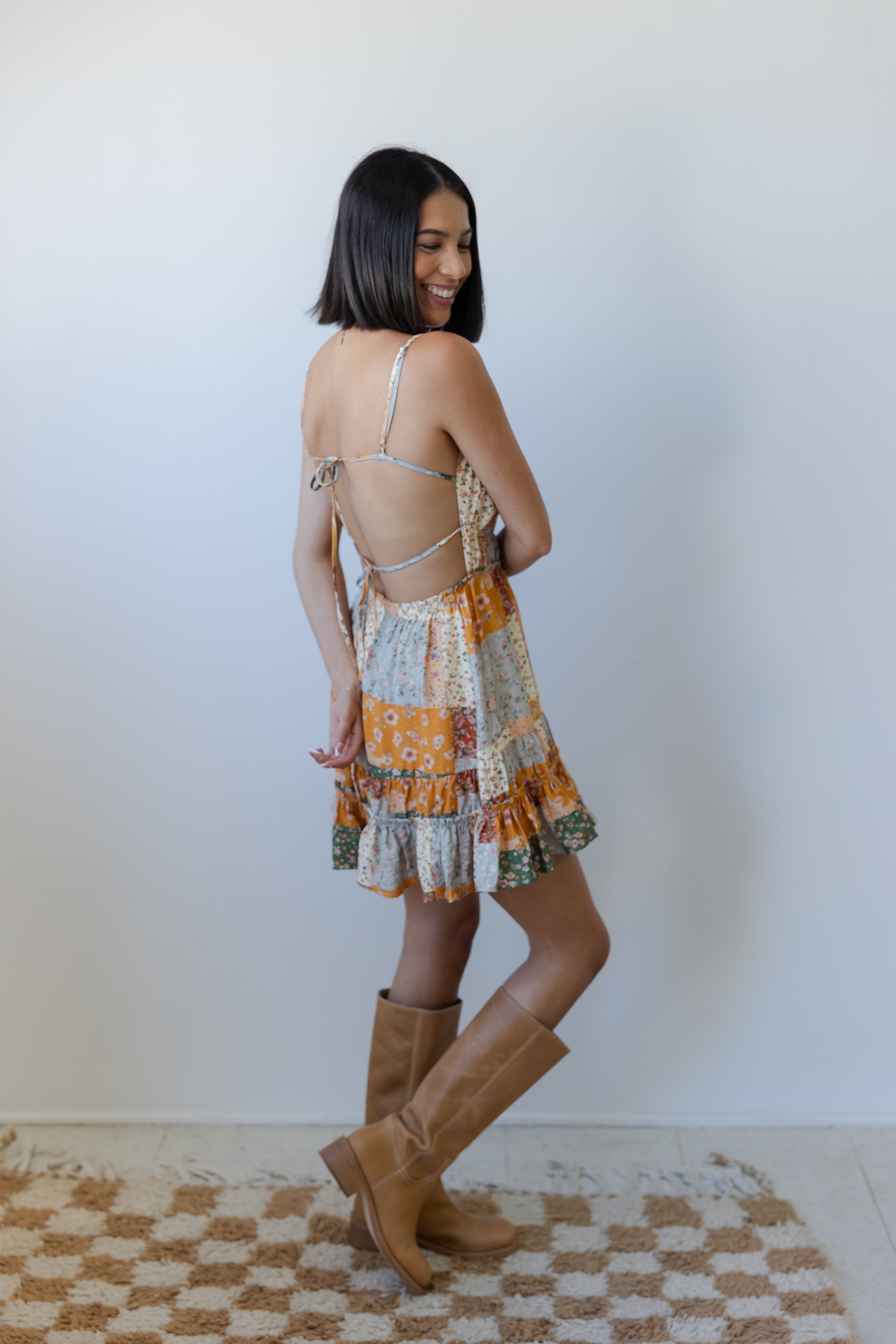 Woman wearing a patterned dress and brown boots standing on a checkered rug.