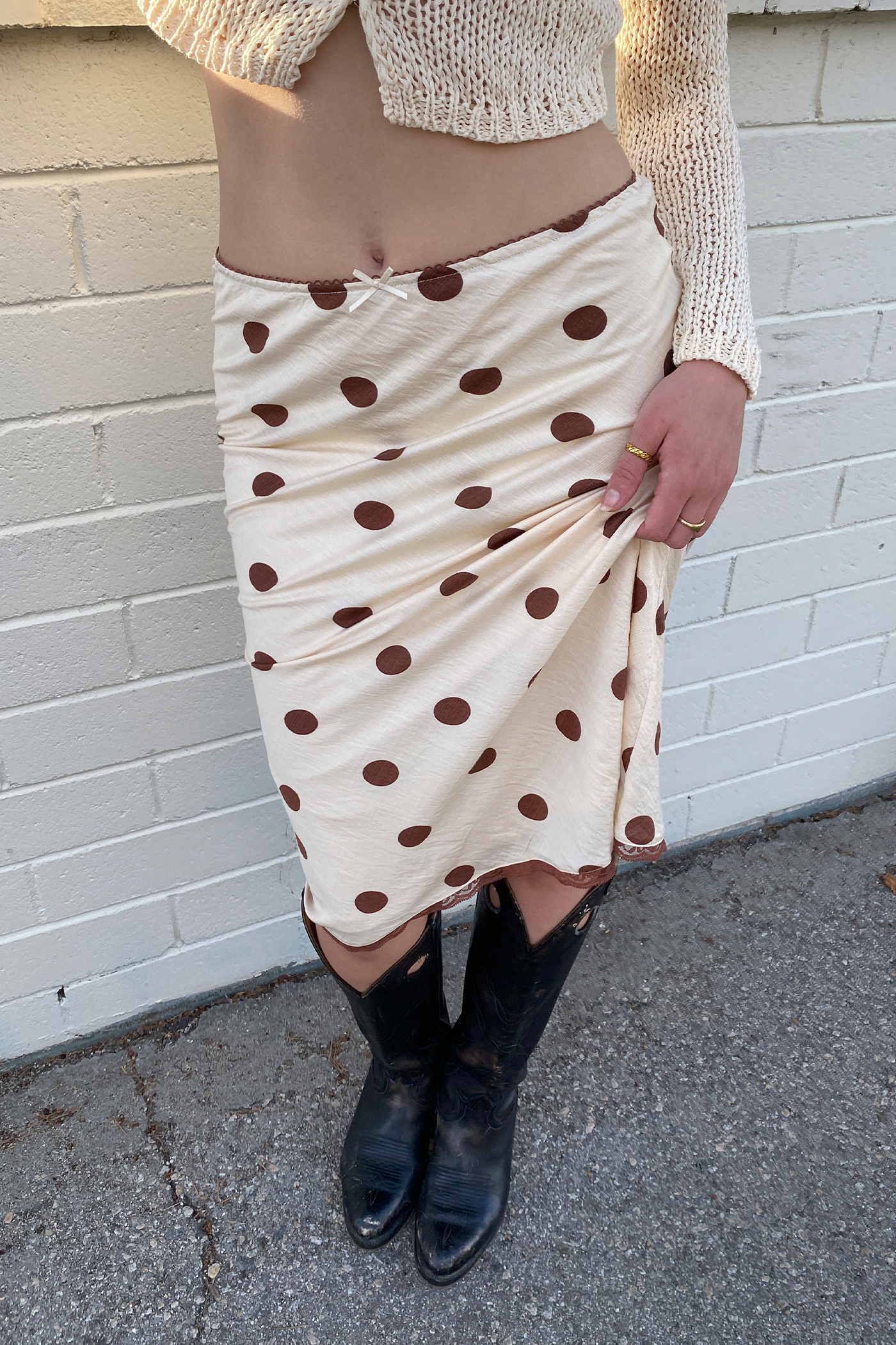 Person wearing a polka dot skirt and black boots against a white brick wall.