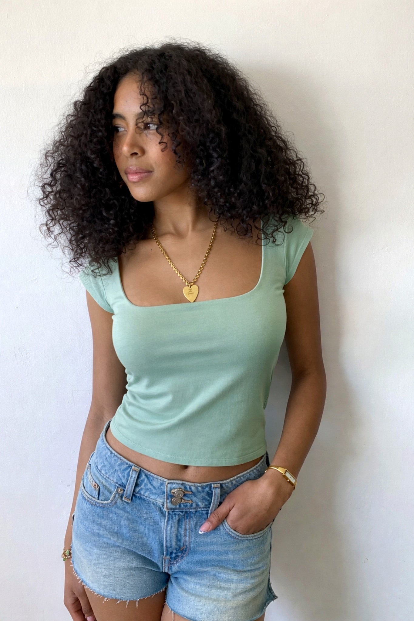 Woman wearing a light green top and denim shorts against a white background