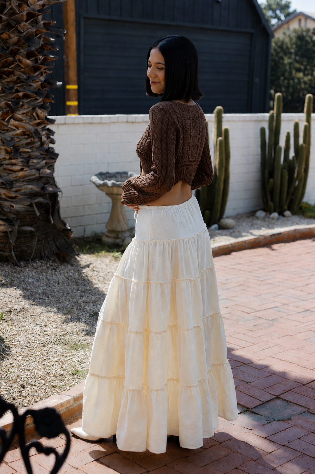 Woman wearing a brown top and white tiered skirt standing outdoors with cacti in the background