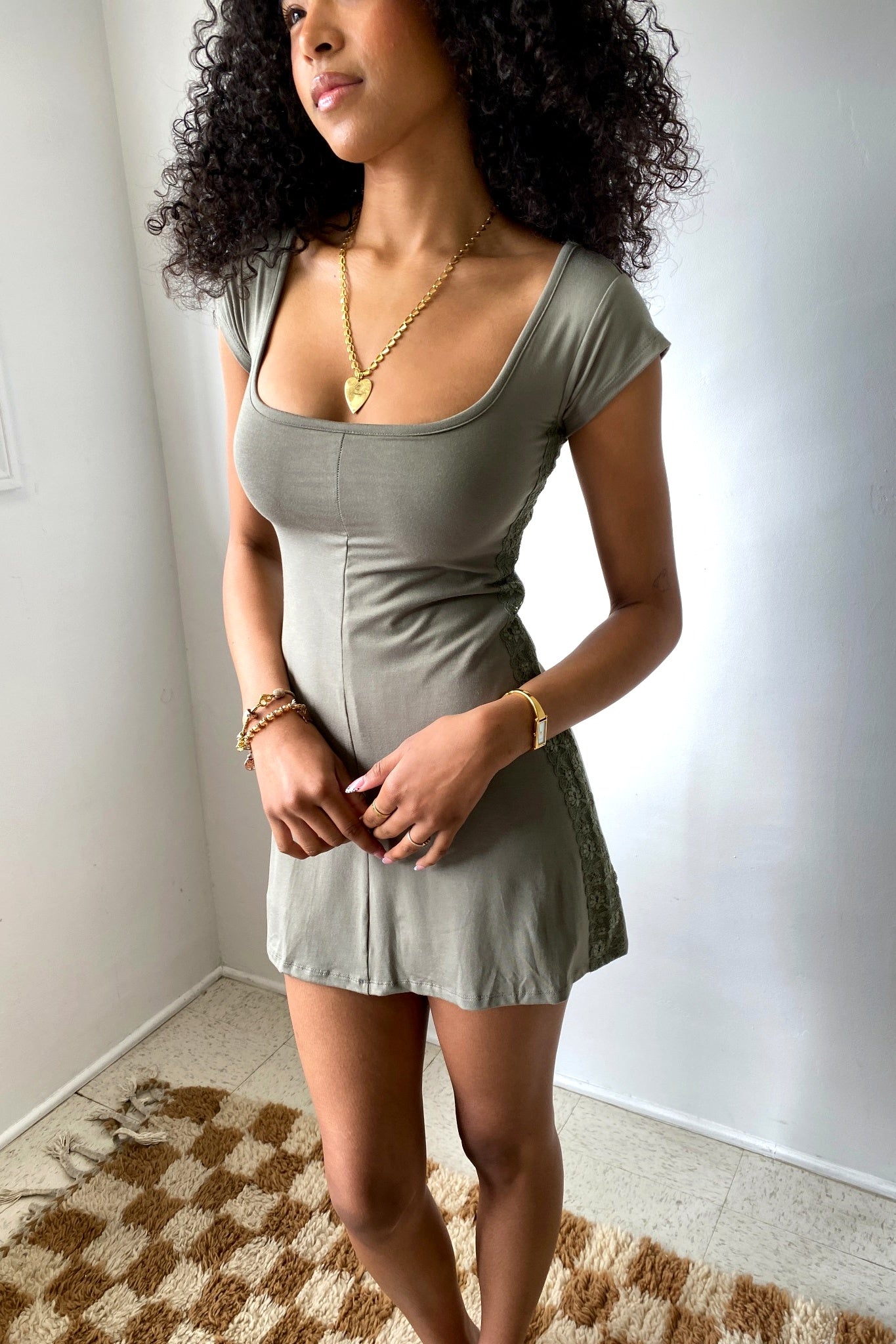Woman wearing a green dress standing in a room with a white wall and patterned rug.