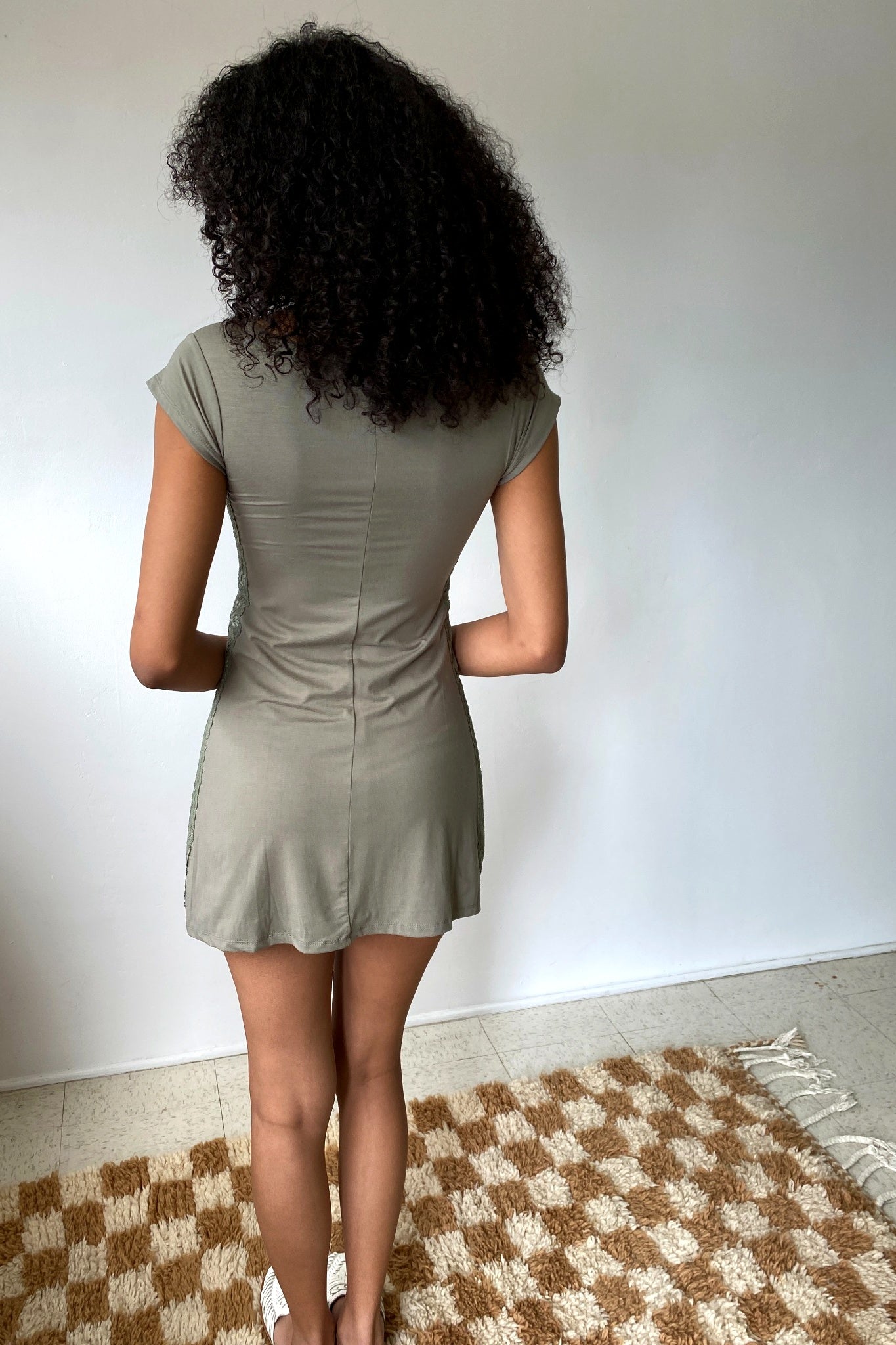 Person wearing a green dress standing on a checkered rug with a plain wall background