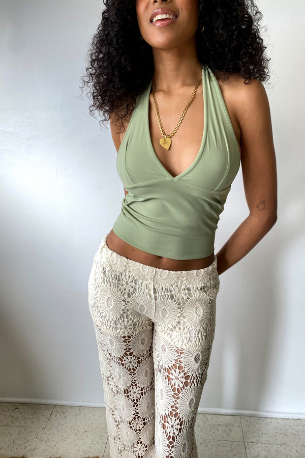 Woman wearing a green top and white lace pants against a plain background