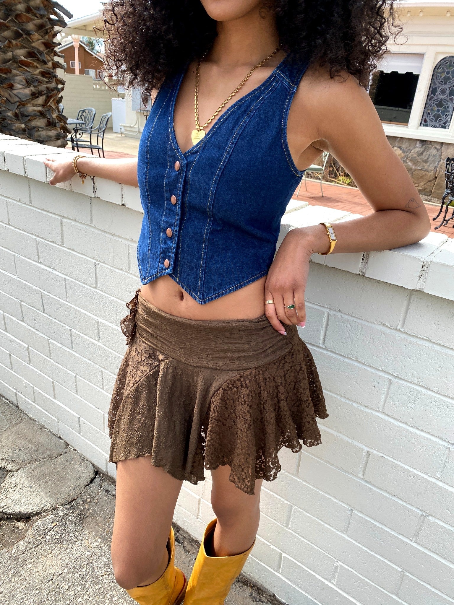 Woman wearing a blue denim top and brown skirt with yellow boots against a white brick wall.