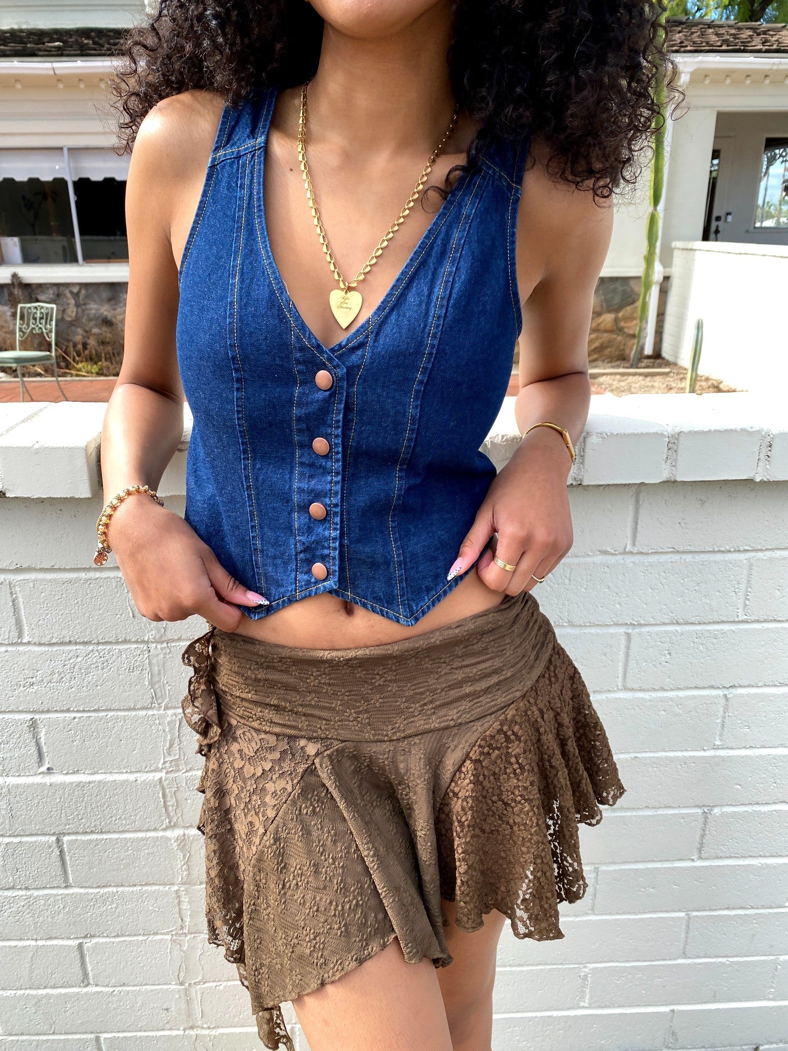 Woman wearing a blue denim top and brown lace skirt against a white brick wall.