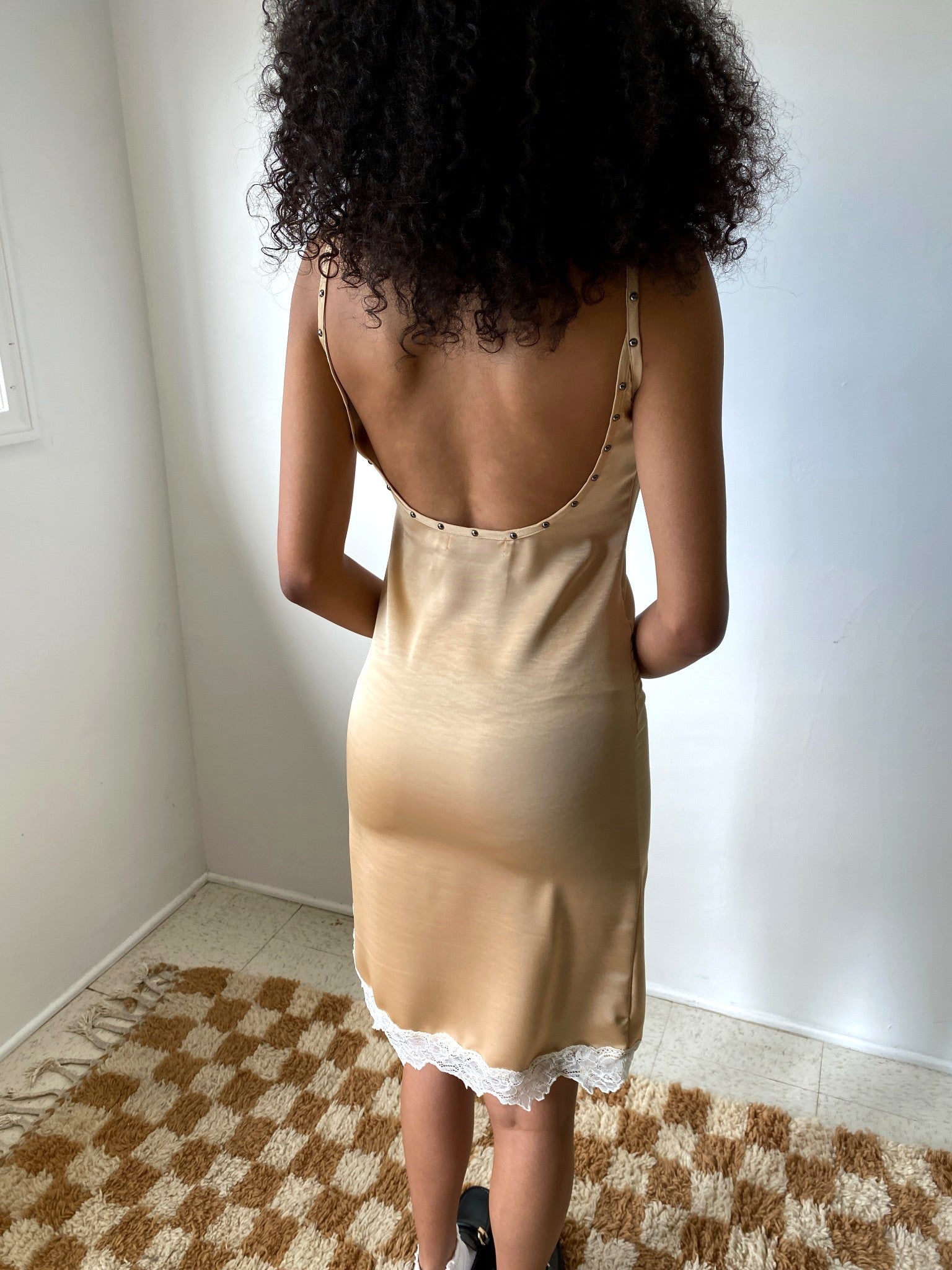 Woman wearing a beige slip dress with lace trim in a room with a checkered rug.
