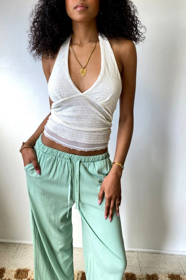 Woman wearing a white halter top and light green pants against a plain background