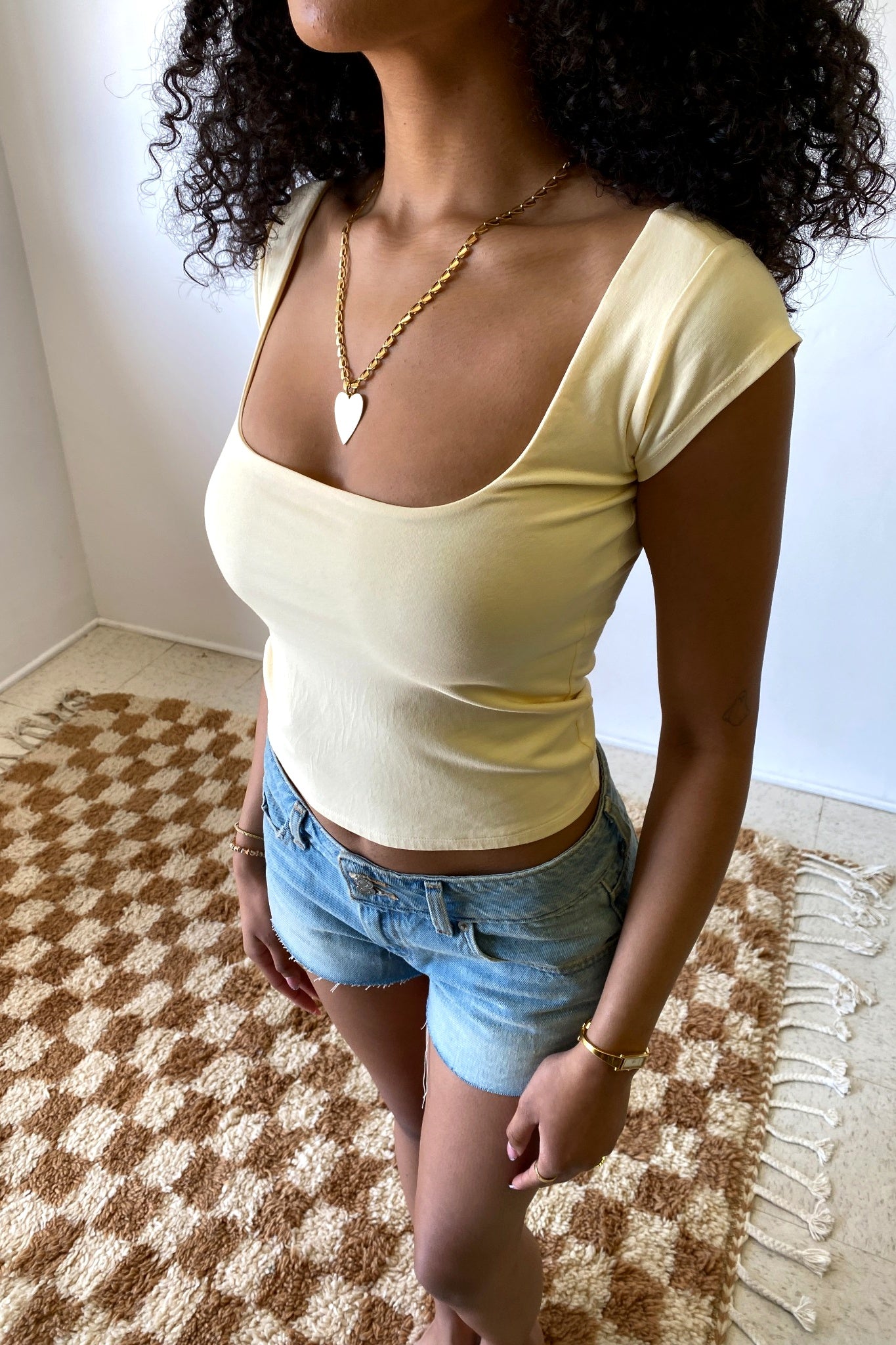 Woman wearing a yellow top and denim shorts on a checkered rug.