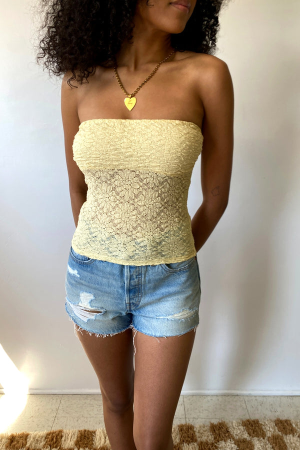 Woman wearing a yellow strapless top and denim shorts against a plain background