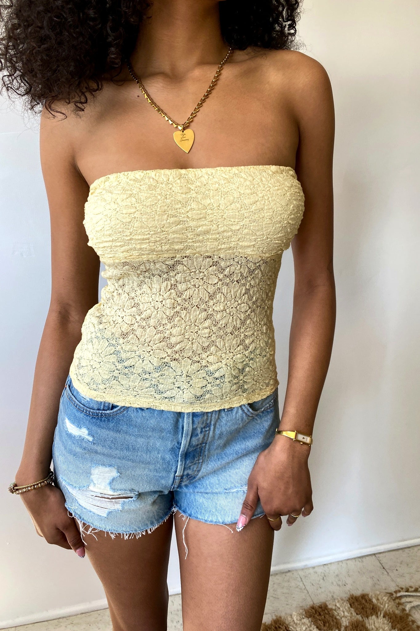 Woman wearing a yellow strapless top and denim shorts against a plain background