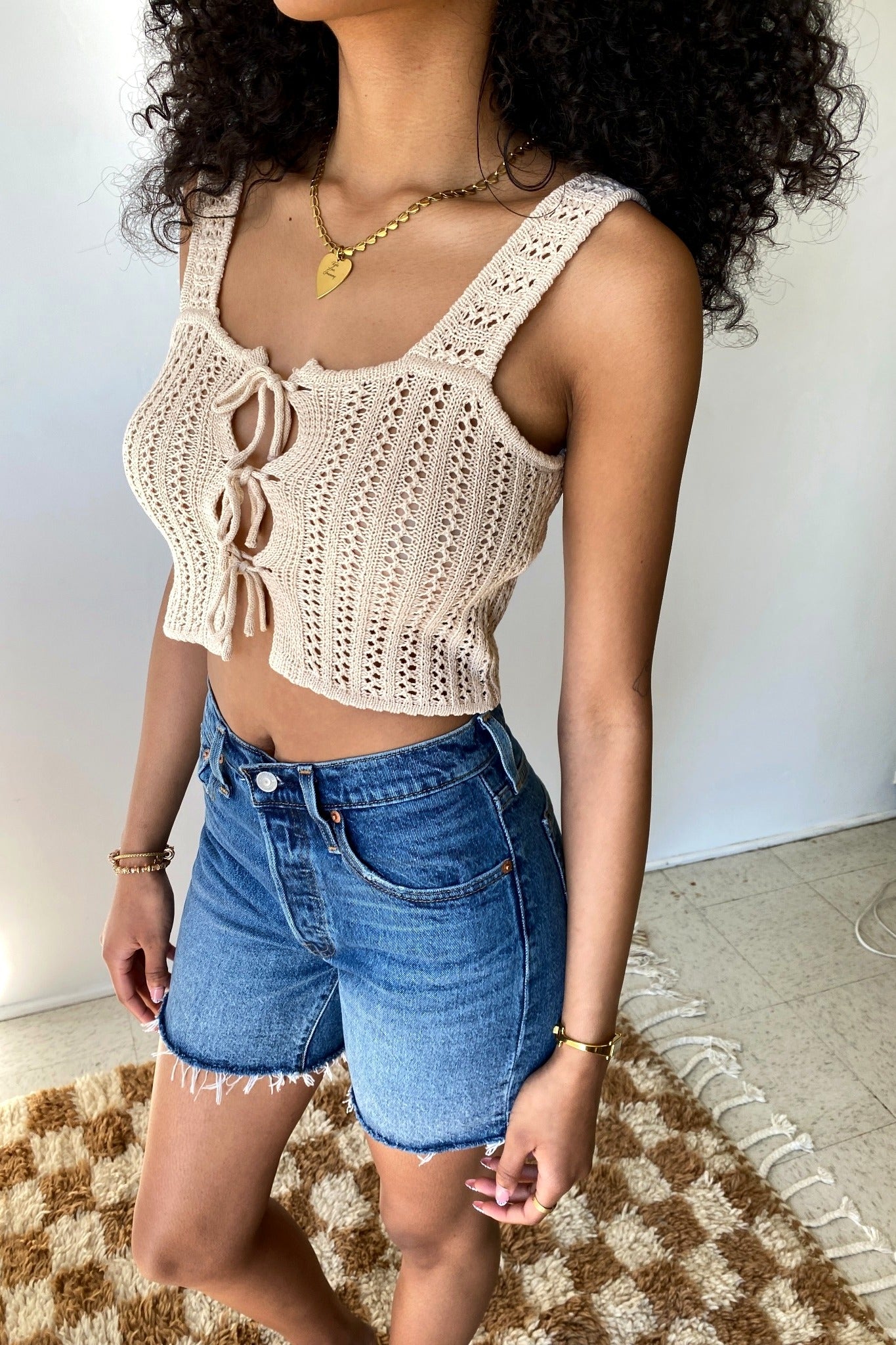 Woman wearing a beige crochet top and denim shorts on a plain background