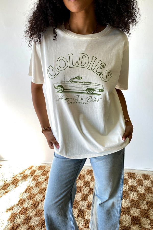 Person wearing a white t-shirt with 'Goldies' graphic design on a plain background