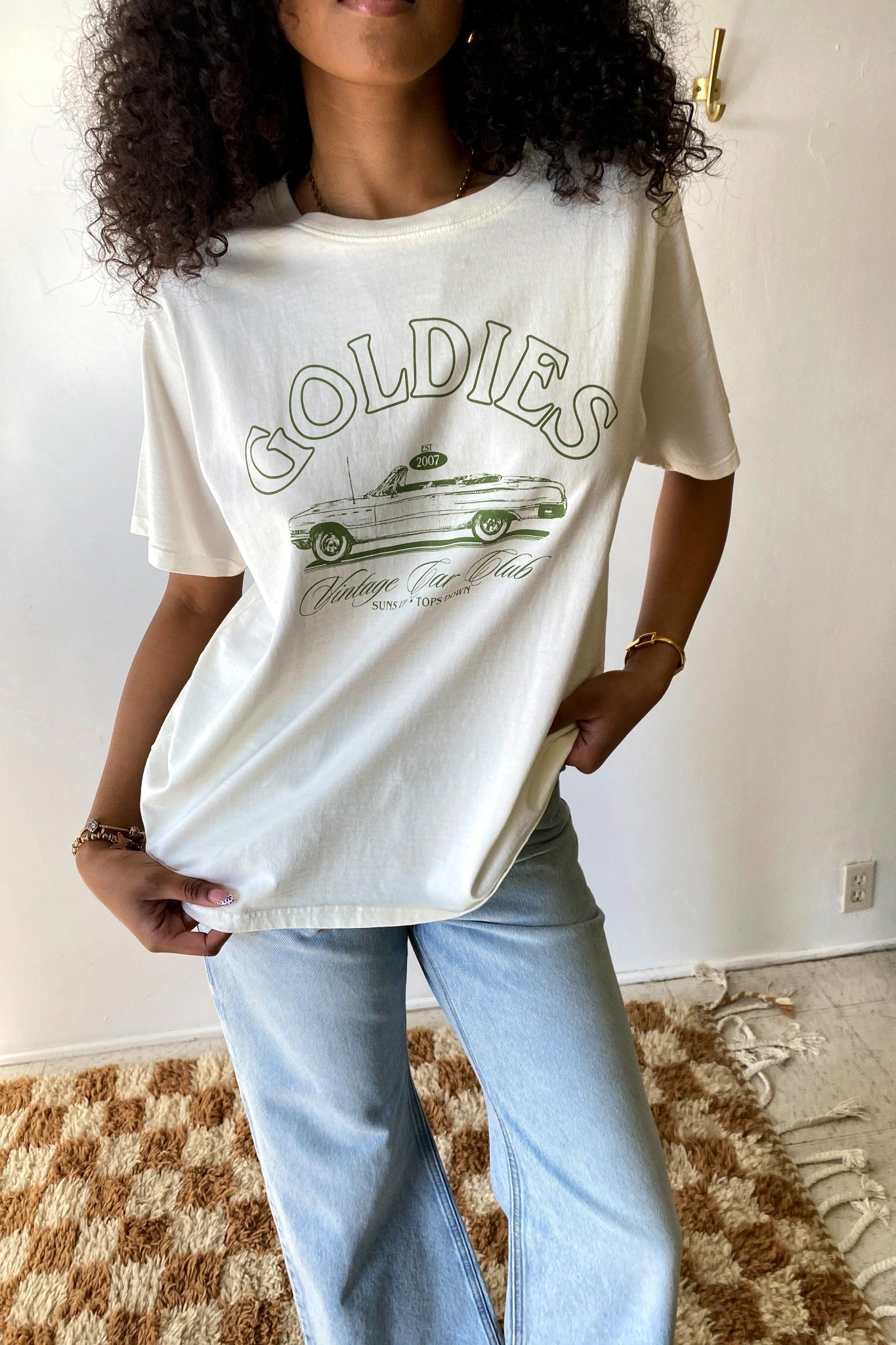 Person wearing a white t-shirt with 'Goldies' graphic design in a casual setting.