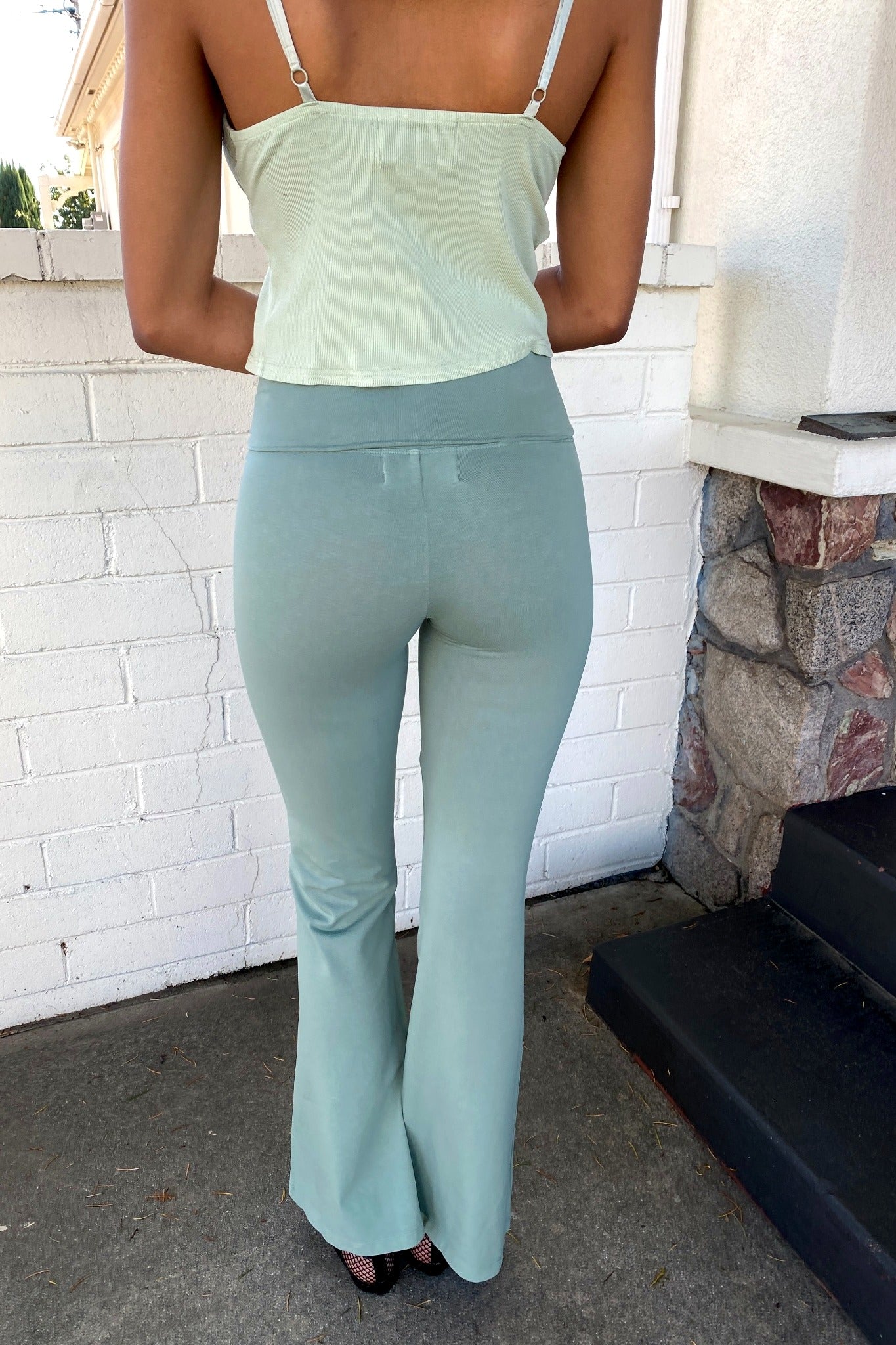 Person wearing a light green top and matching flared pants standing in front of a white brick wall.