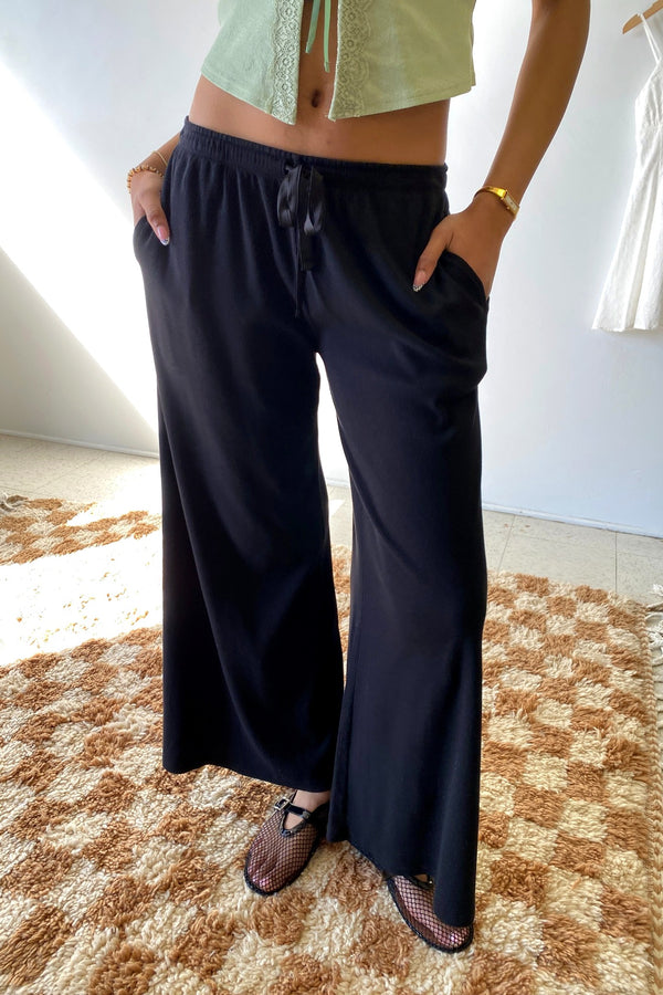 Person wearing black wide-leg pants and a light green top on a checkered floor.