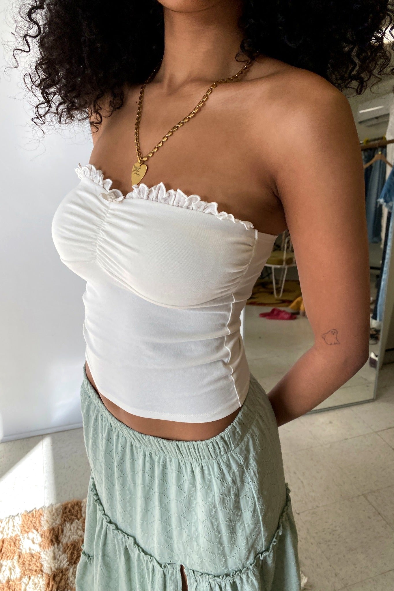 Woman wearing a white off-shoulder top and light green skirt indoors.