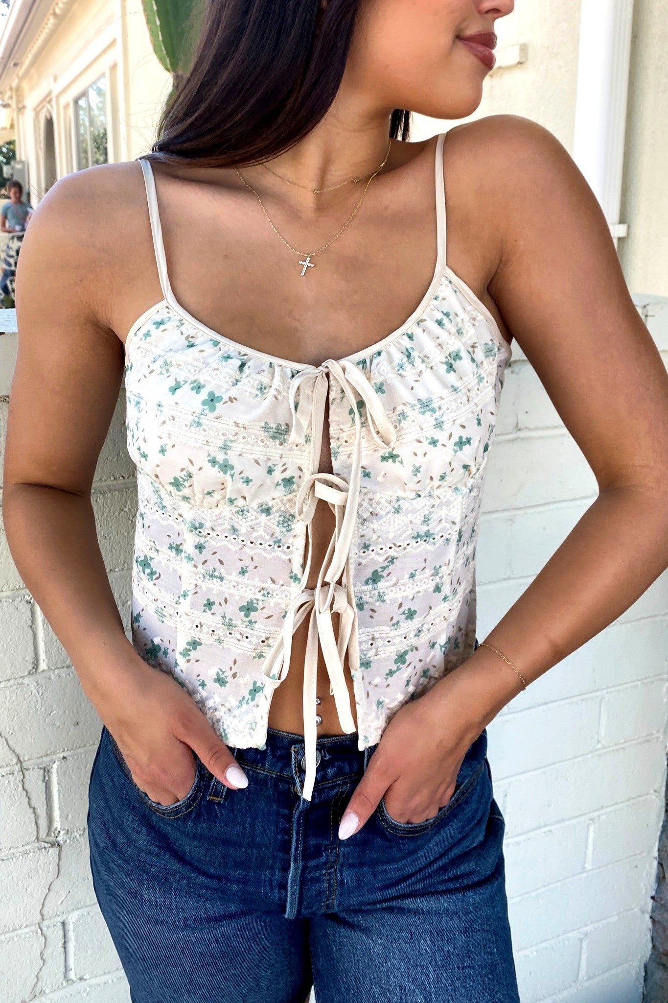 Woman wearing a floral camisole top with a white brick wall background