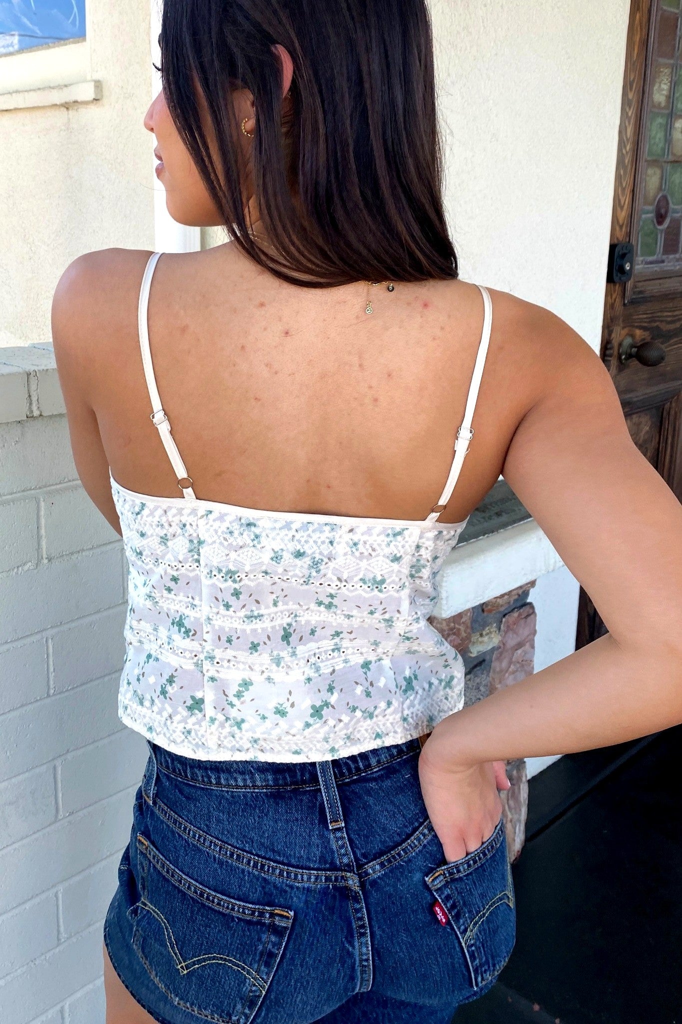 Person wearing a floral top and denim shorts with a neutral background