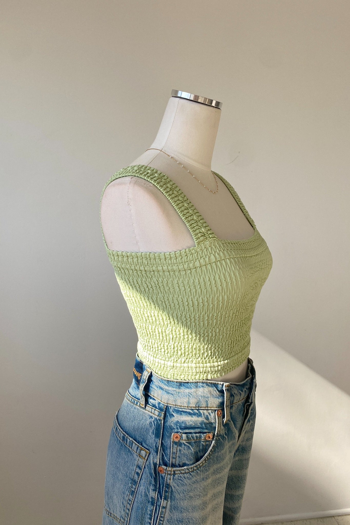 Mannequin wearing a light green textured top and blue jeans against a plain background