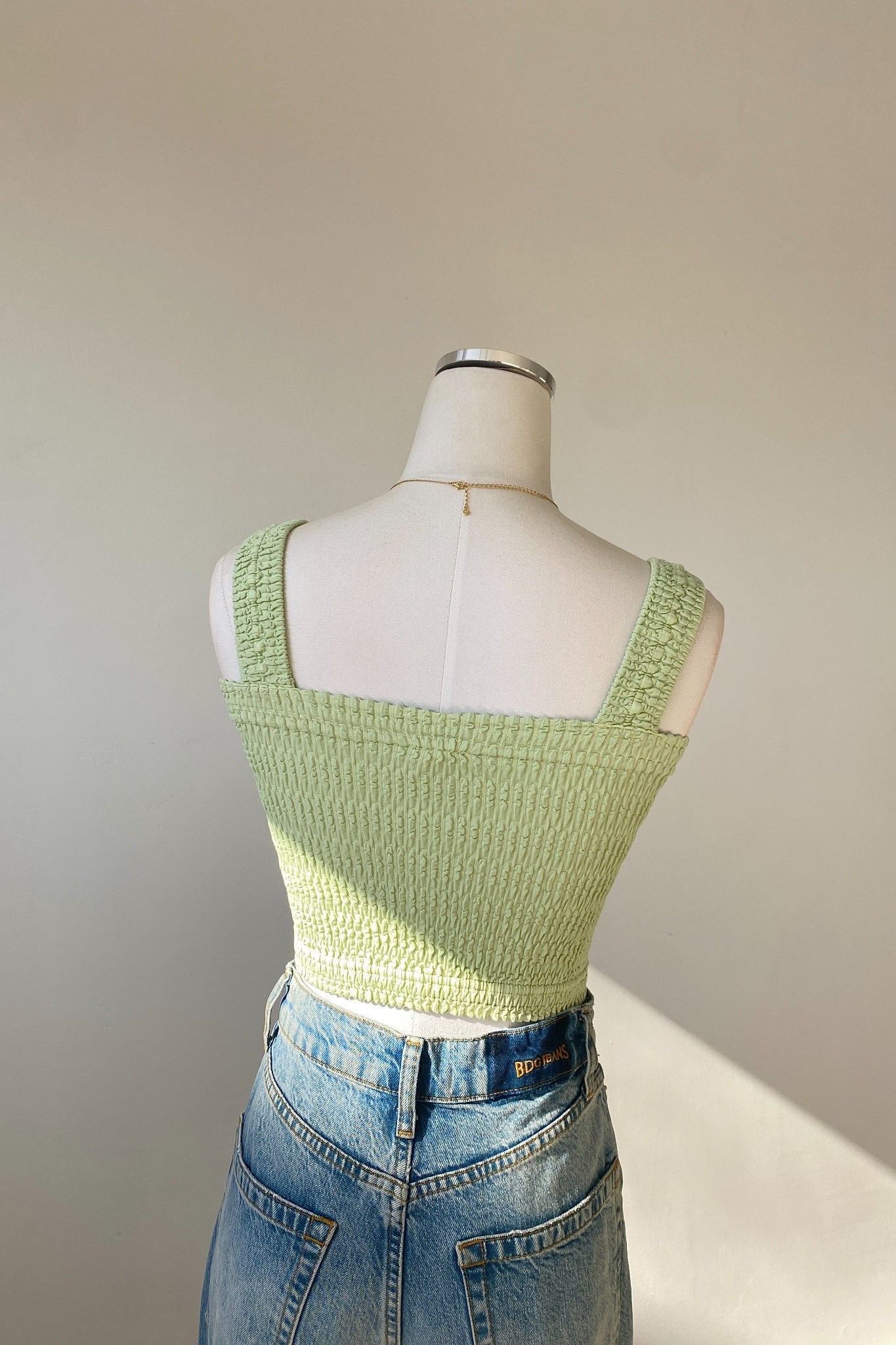 Mannequin wearing a light green knitted top and blue jeans against a plain background