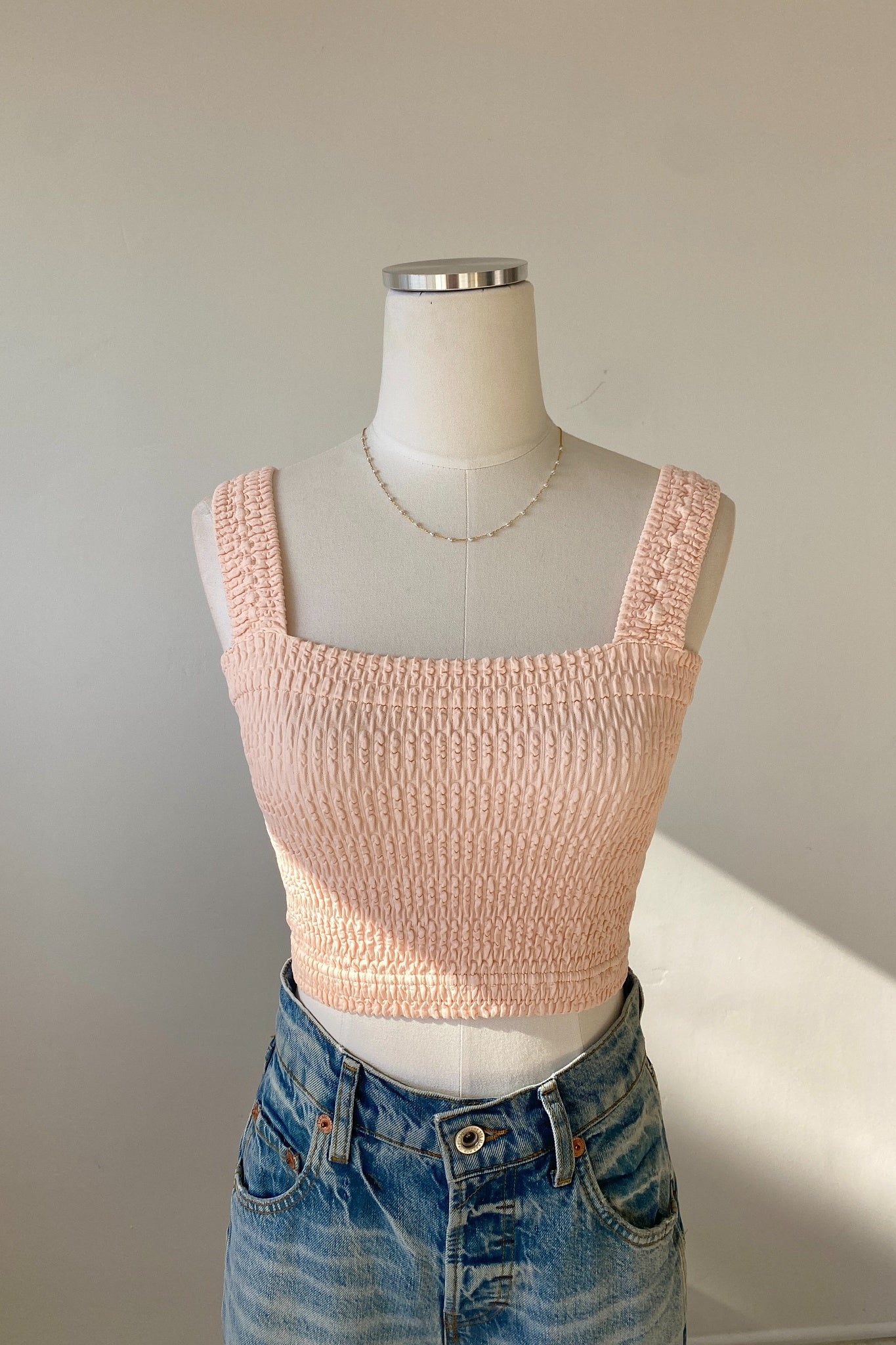 Mannequin wearing a pink knitted crop top and blue jeans against a neutral background
