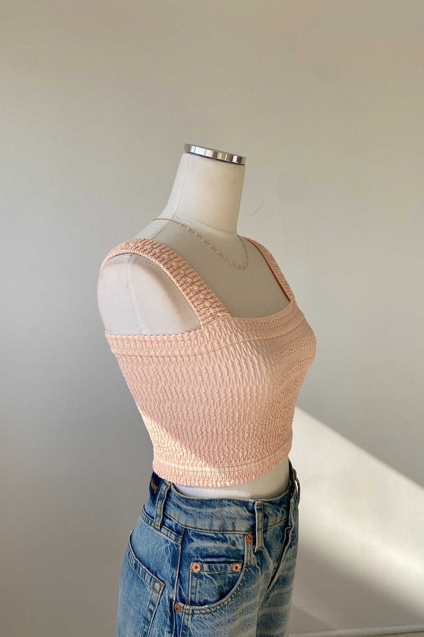 Mannequin wearing a pink textured top and blue jeans against a plain background