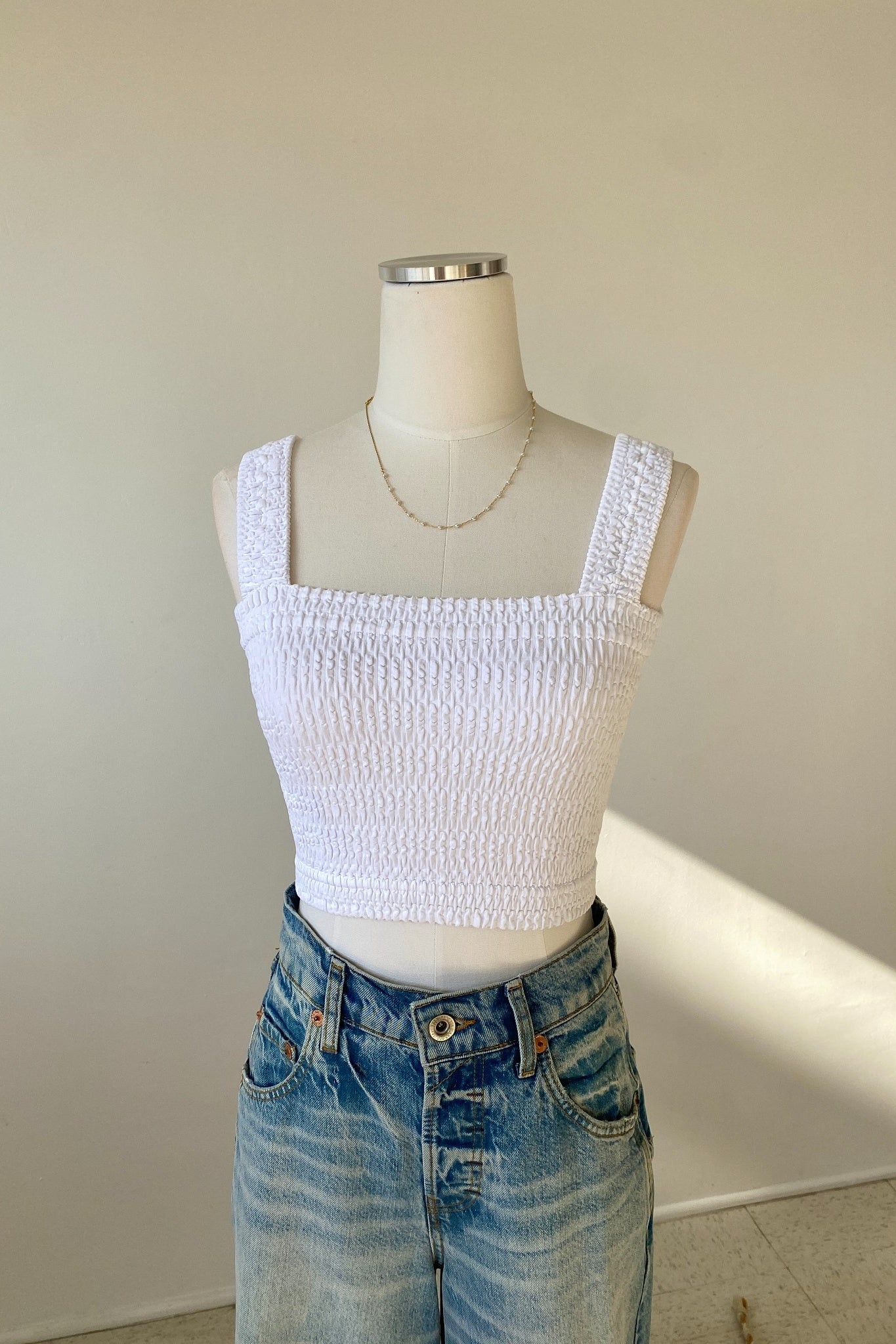 White textured crop top on a mannequin with blue jeans against a plain background