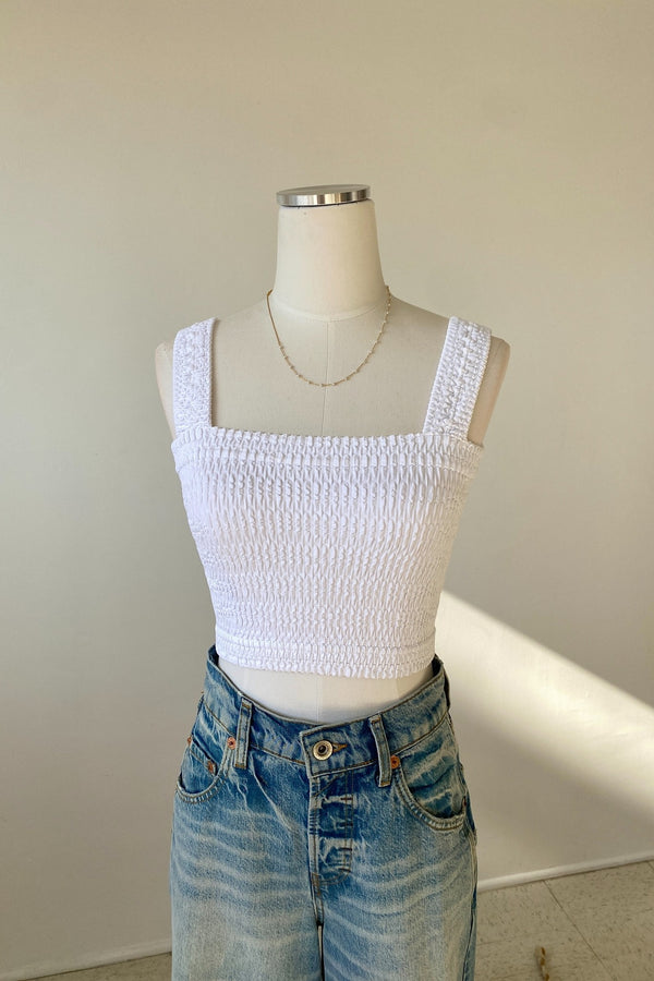 White textured crop top on a mannequin with blue jeans against a plain background